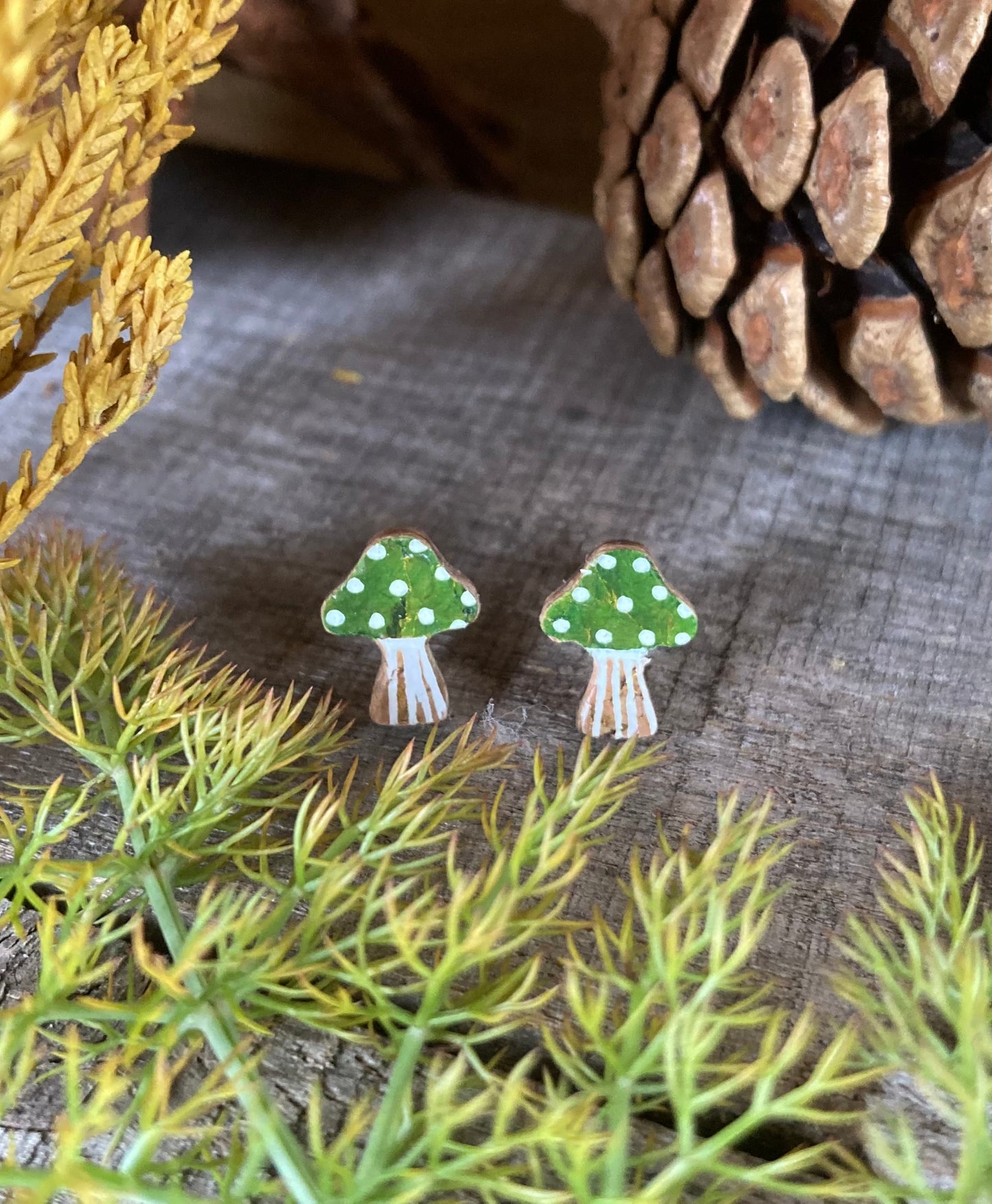 Green mushroom earrings with white polka dots on a textured surface with foliage.