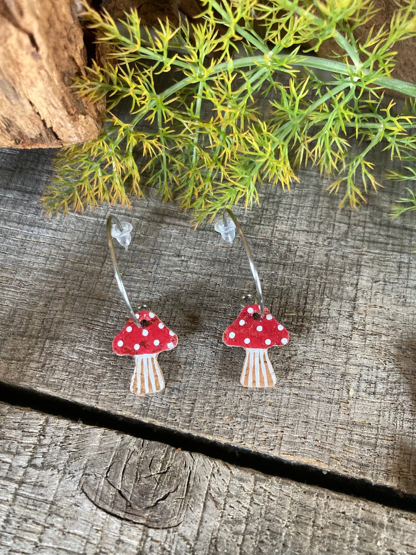 Mushroom-shaped earrings on a wooden surface with greenery in the background