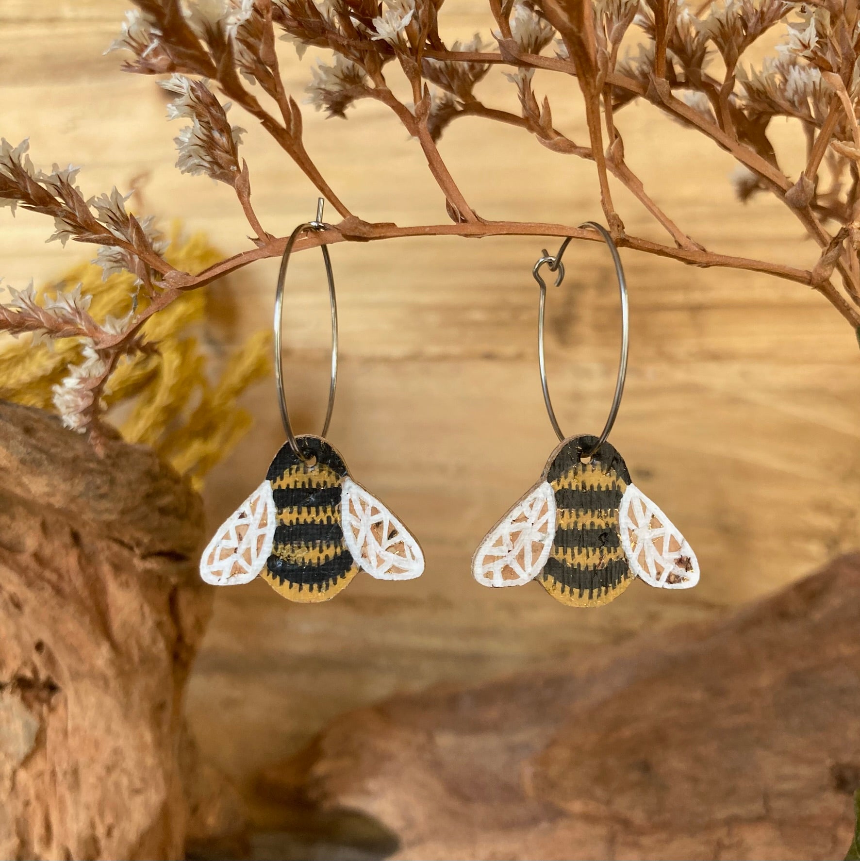 Bee-shaped earrings hanging on a branch with a natural background