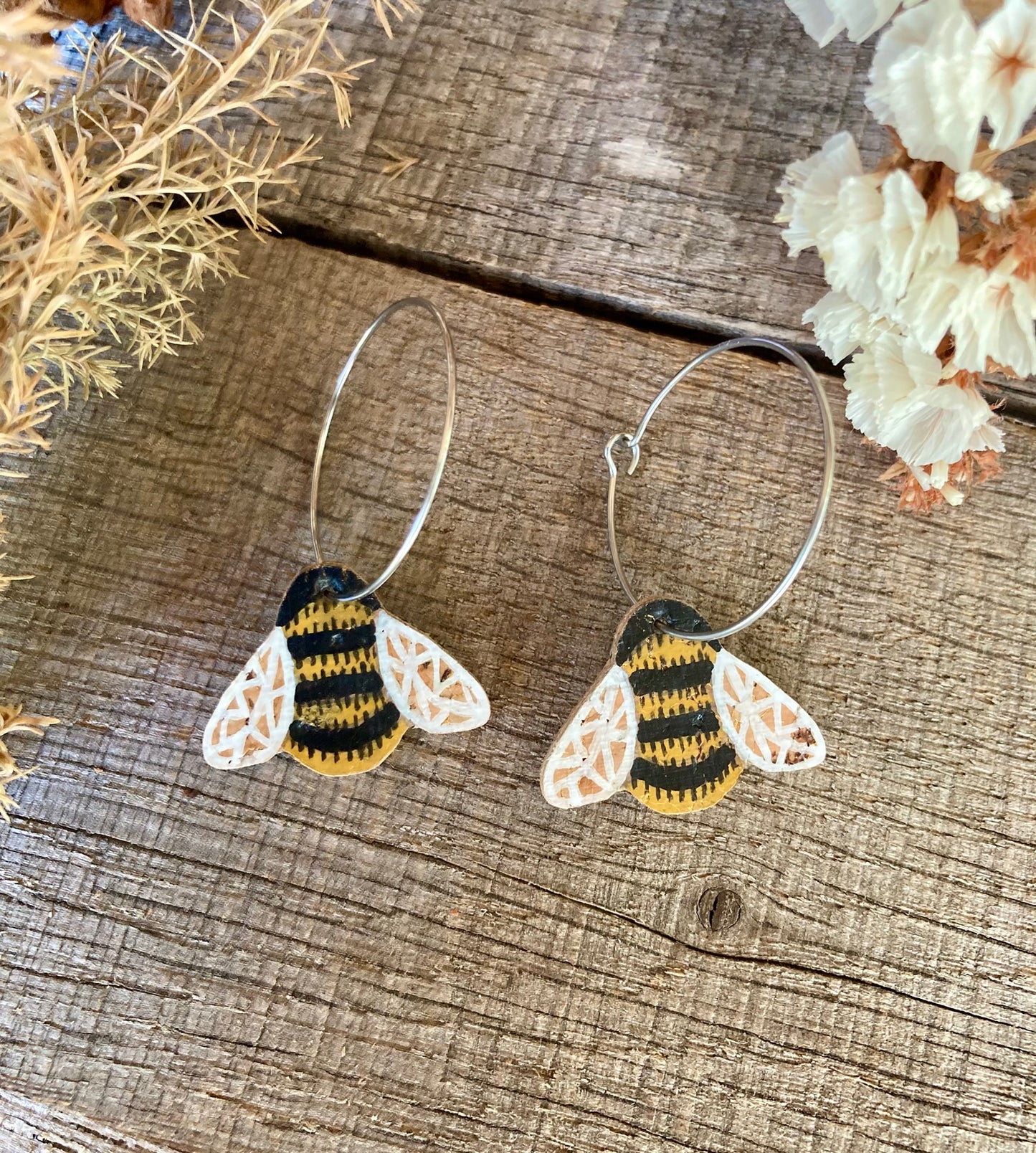 Bee-shaped earrings on a wooden surface with flowers in the background