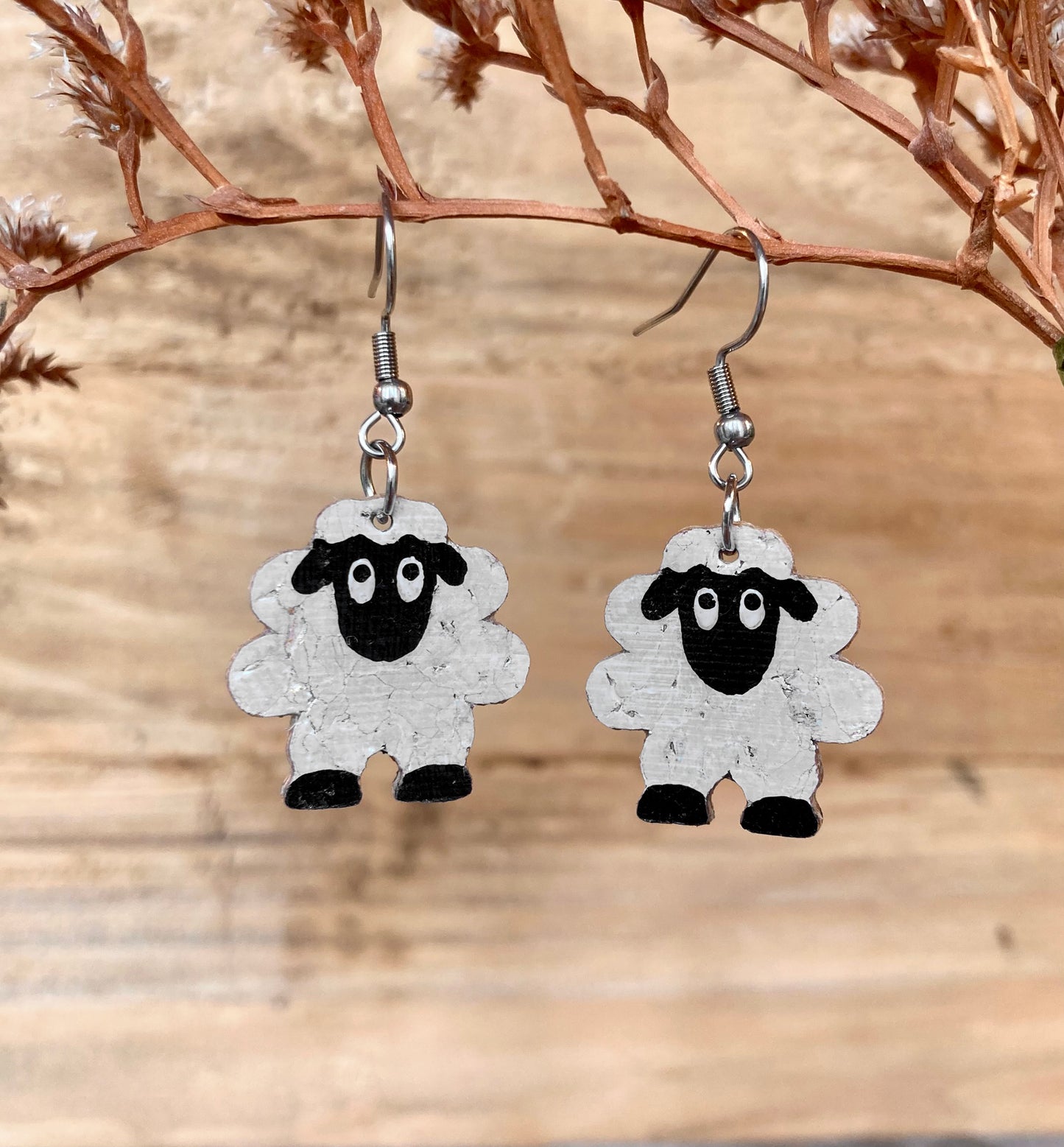 Sheep-shaped earrings hanging on a branch with a wooden background