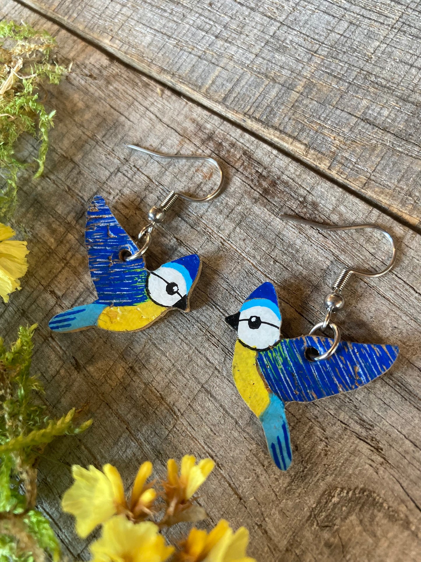 Bird-shaped earrings on a wooden surface with yellow flowers.