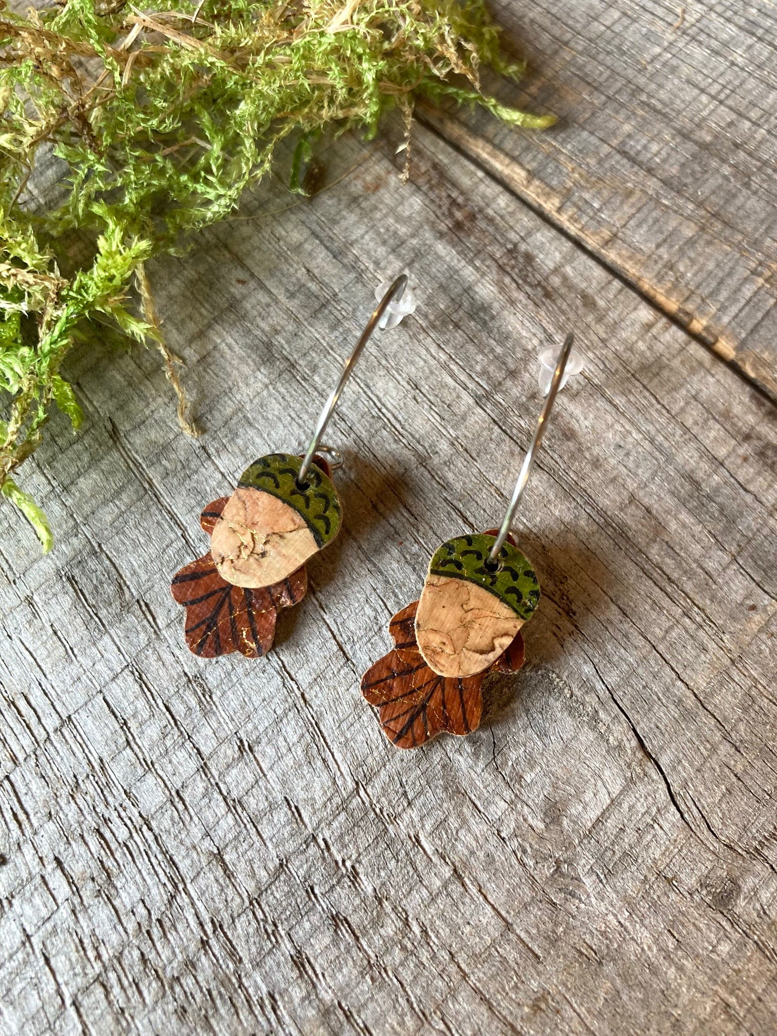 Pair of earrings with acorn and leaf designs on a wooden surface