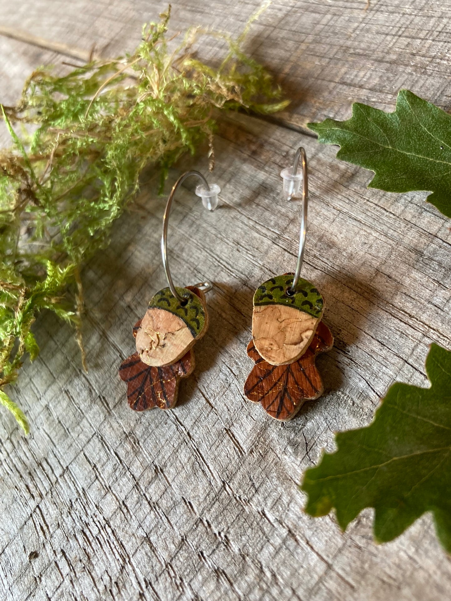 Pair of acorn-shaped earrings on a wooden surface with leaves.