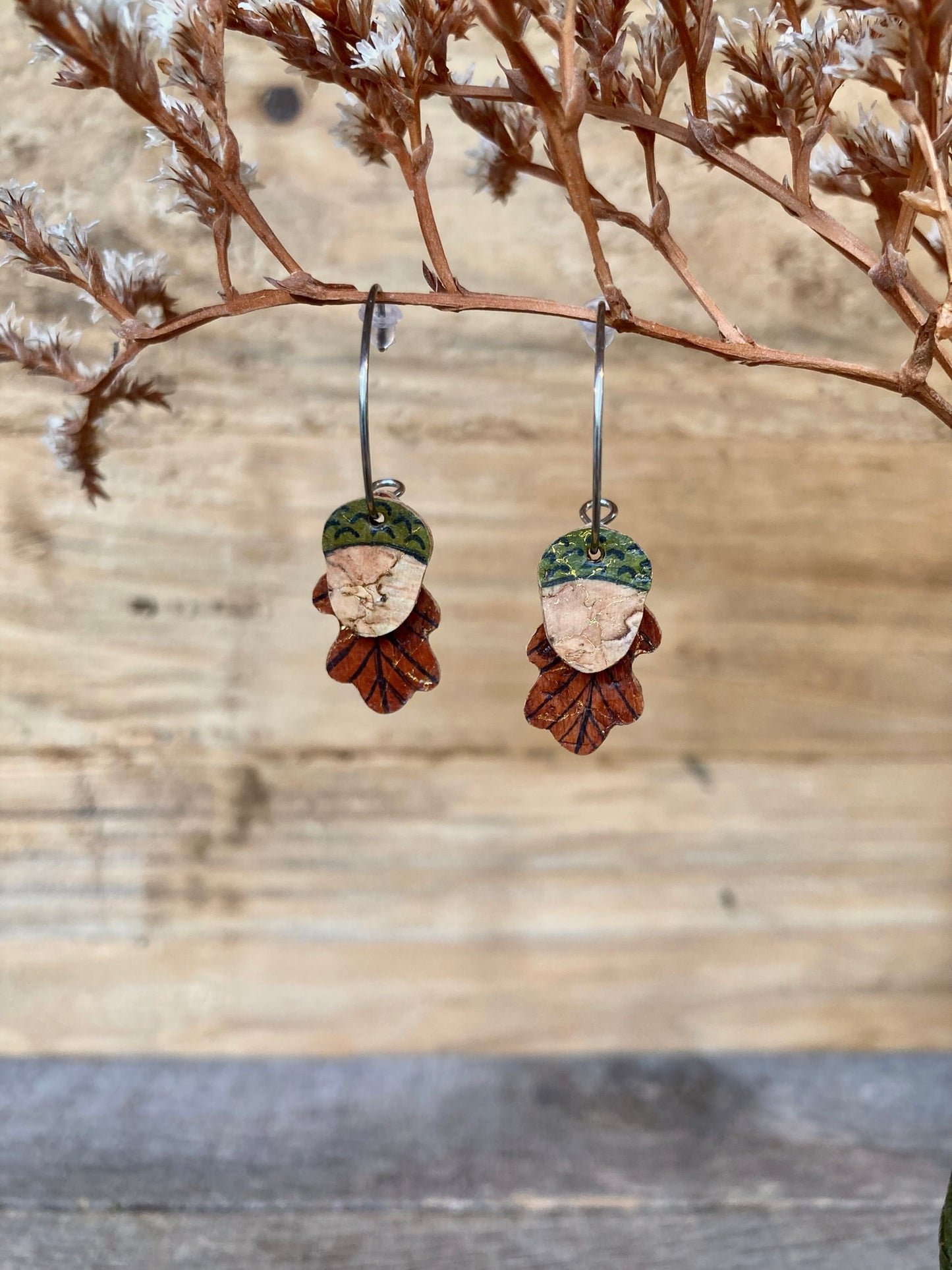 Pair of earrings with a acorn and leaf design hanging on a branch.