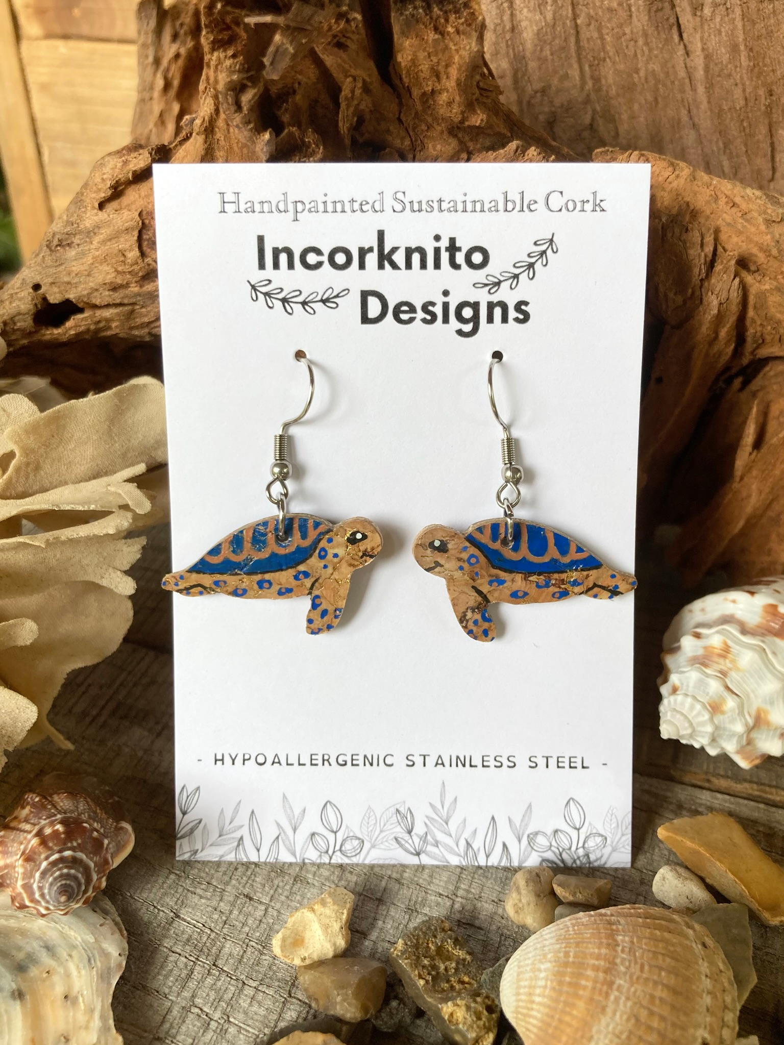 Turtle-shaped earrings on a card with 'Incorknito Designs' branding, surrounded by natural elements.