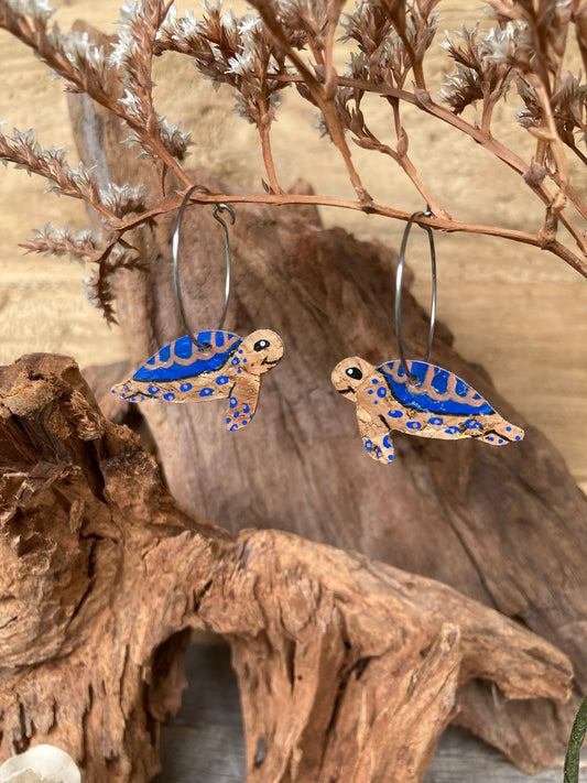 Turtle-shaped cork earrings with blue accents on a wooden surface