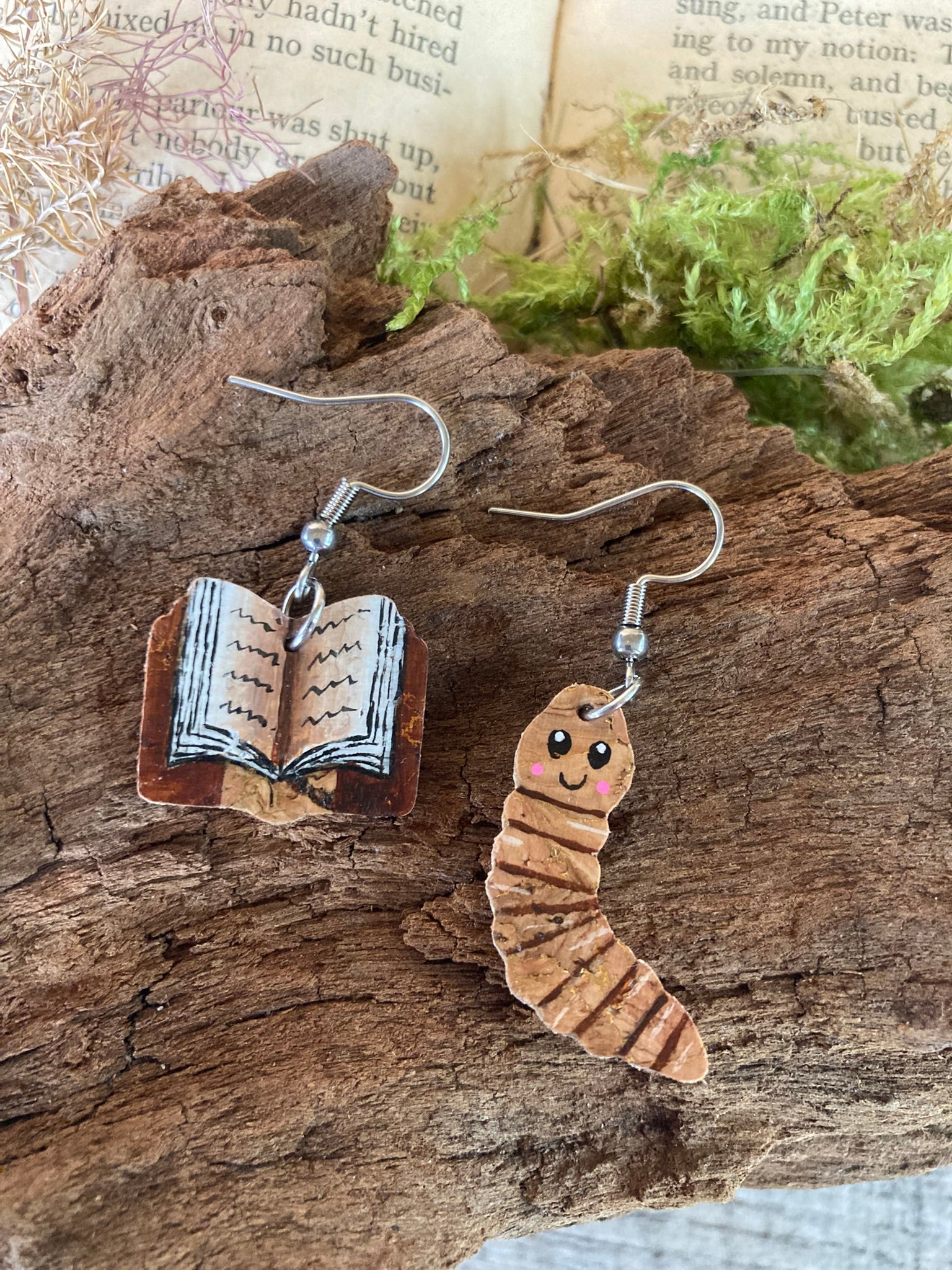 Two unique earrings shaped like a book and a worm on a wooden surface