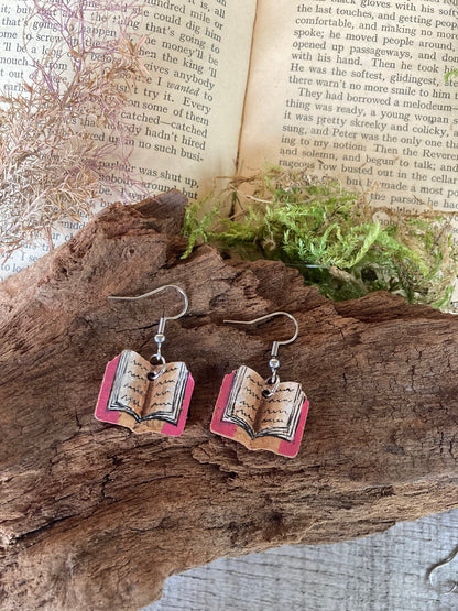 Book-shaped earrings on a wooden surface with an open book in the background