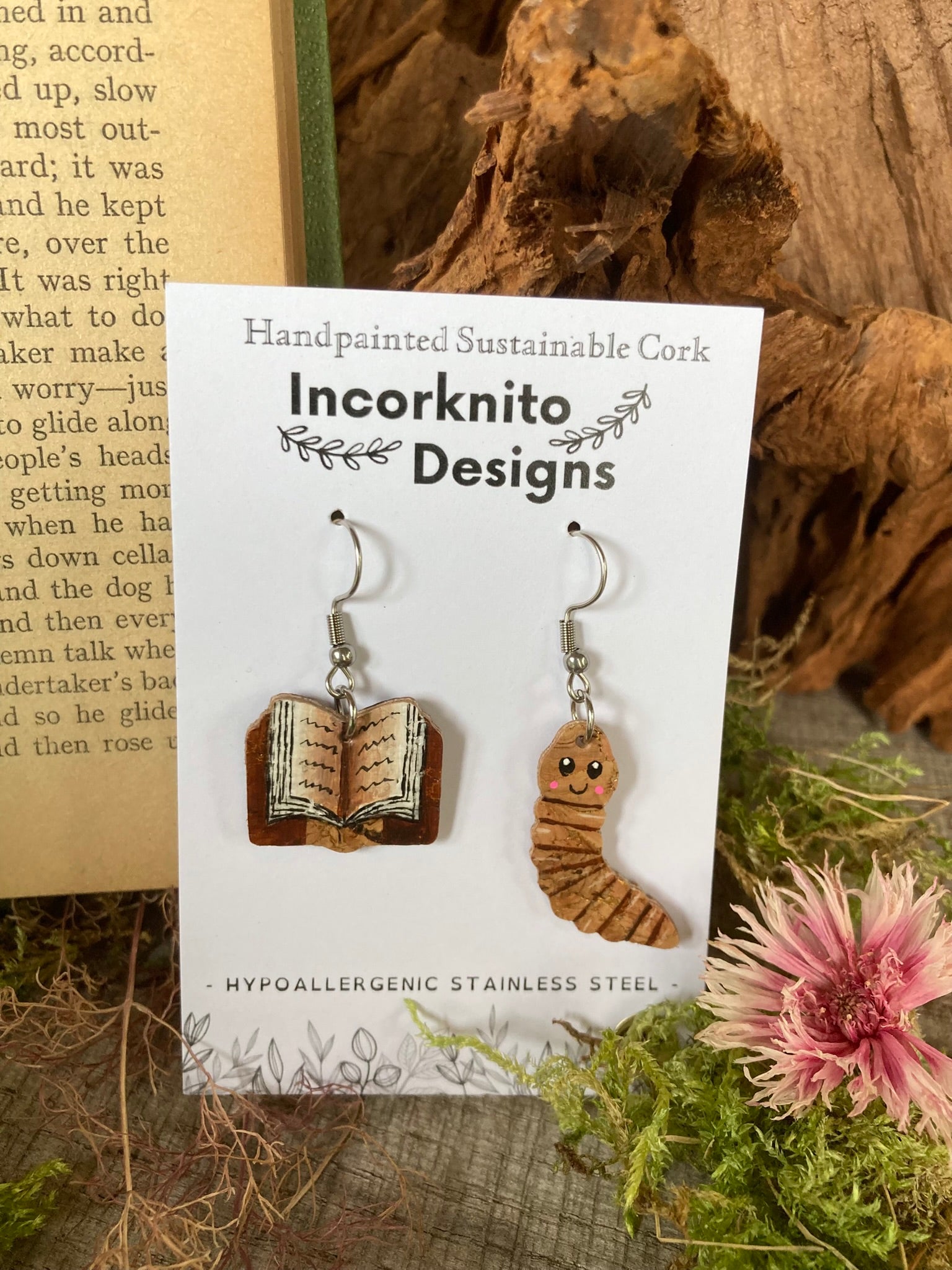 Mismatched cork earrings (one book and one worm - to read as bookworm) on a card with 'Incorknito Designs' branding, placed on a natural background.