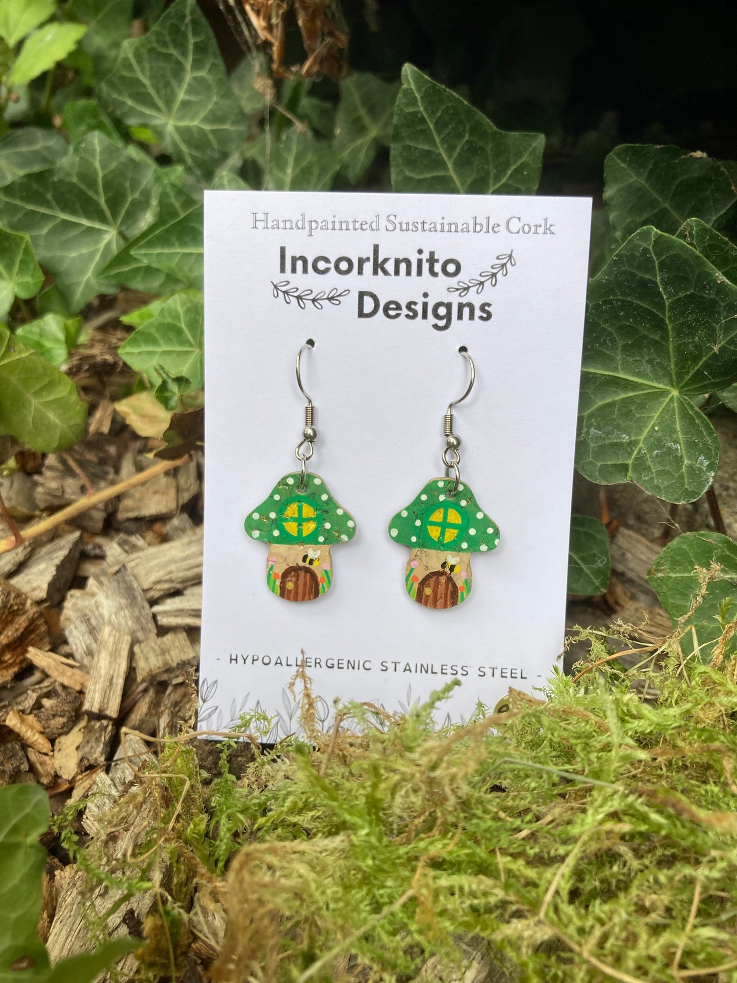 Mushroom-shaped earrings on a 'Incorknito Designs' card with green leaves in the background