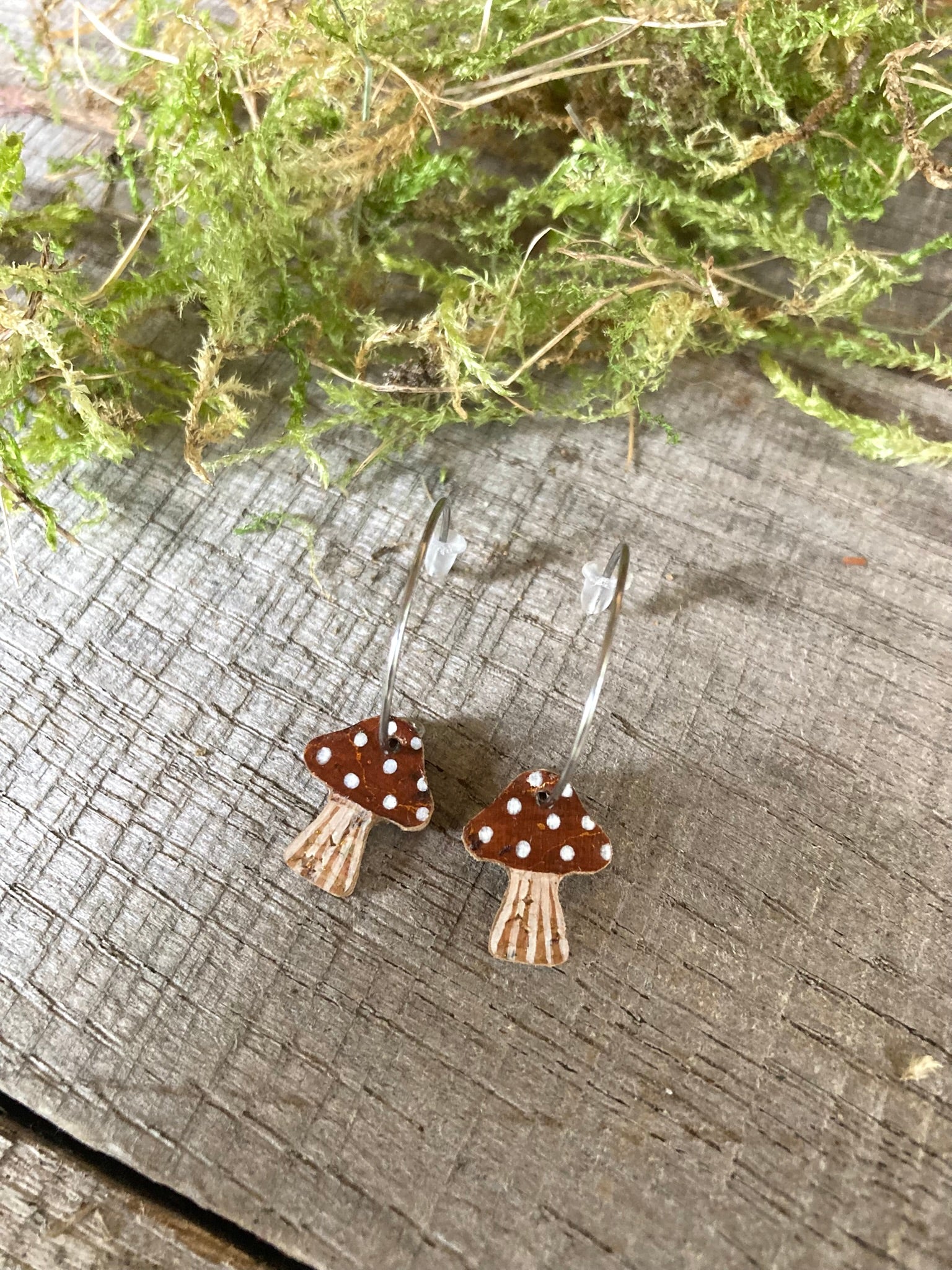 Mushroom-shaped earrings on a wooden surface with greenery in the background