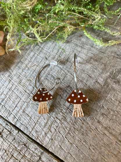 brown spotted toadstool-shaped earrings on a wooden surface with greenery in the background