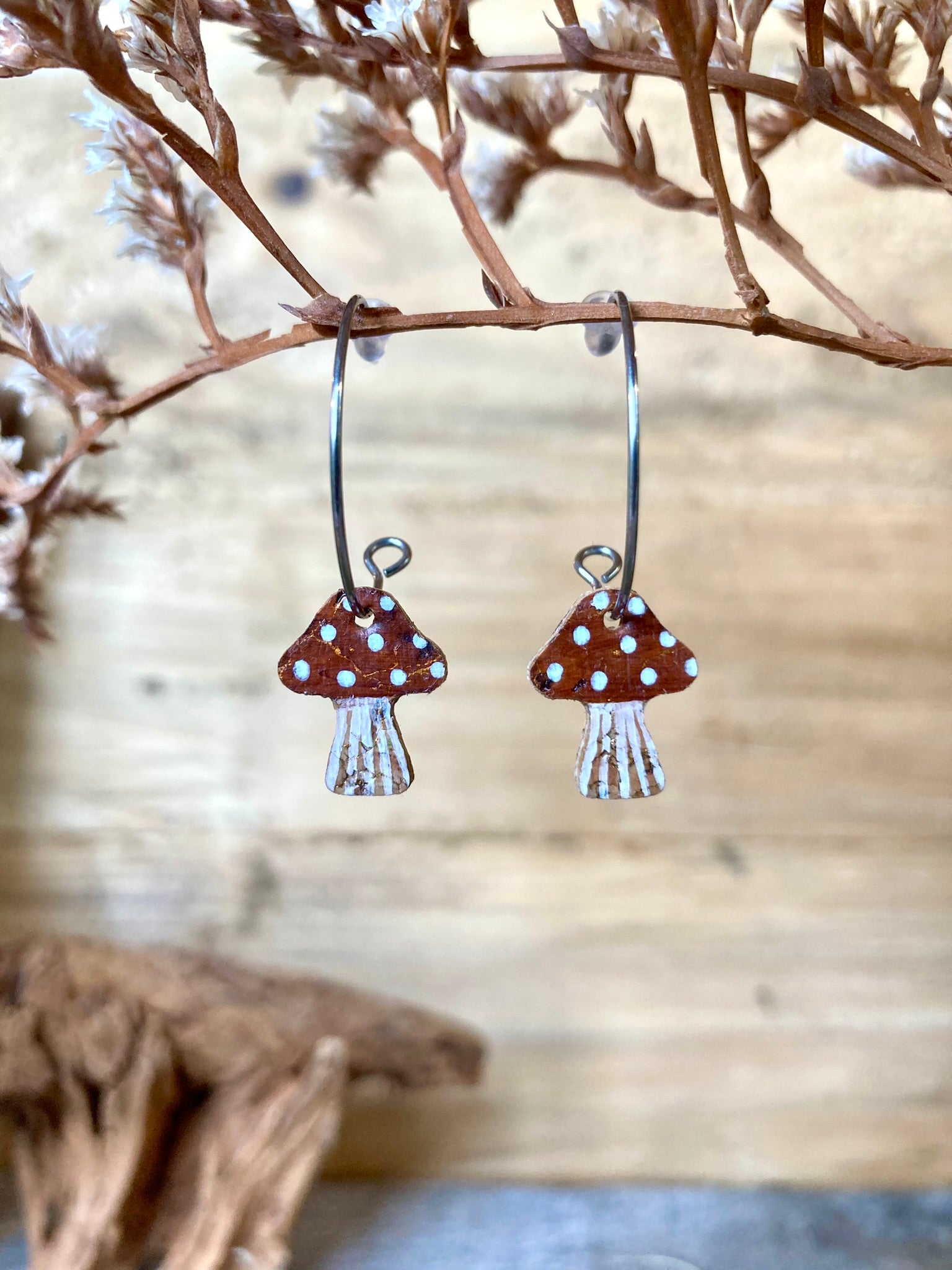 Brown mushroom-shaped earrings hanging from a branch with a natural background