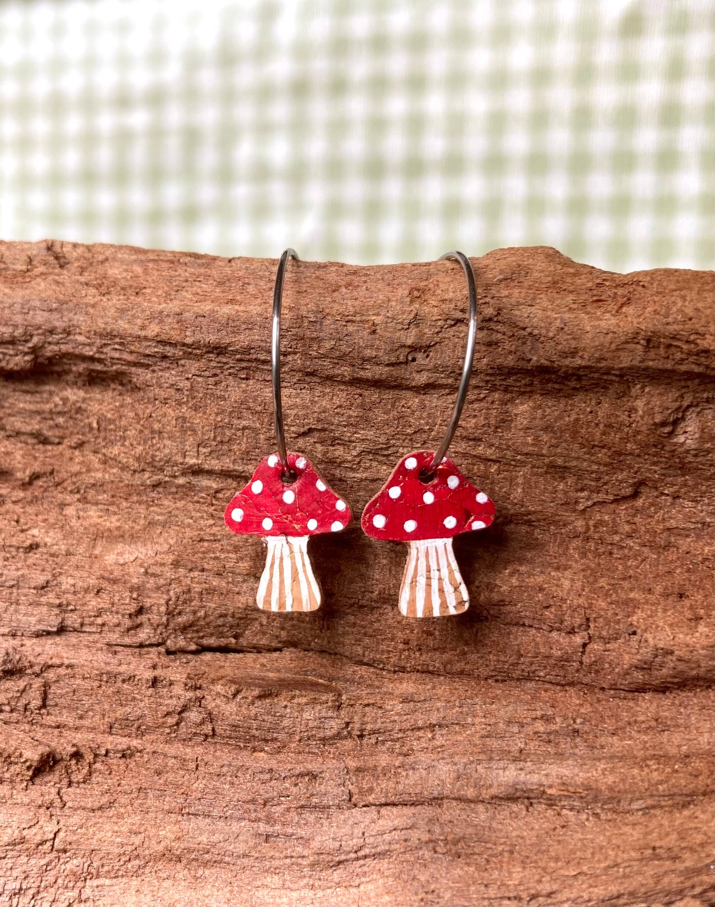 Mushroom-shaped earrings with red caps and white spots on a wooden surface.
