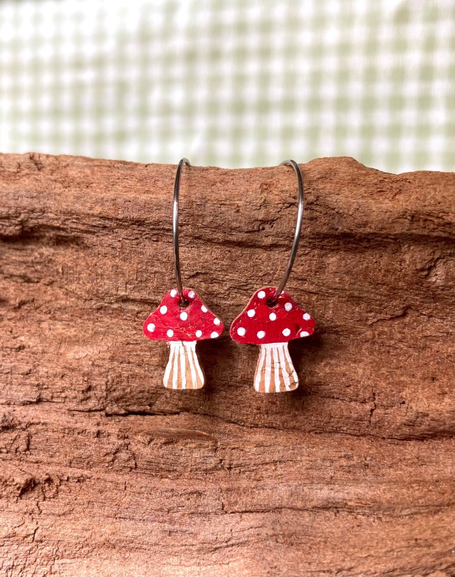 Mushroom-shaped earrings with red caps and white spots on a wooden surface.
