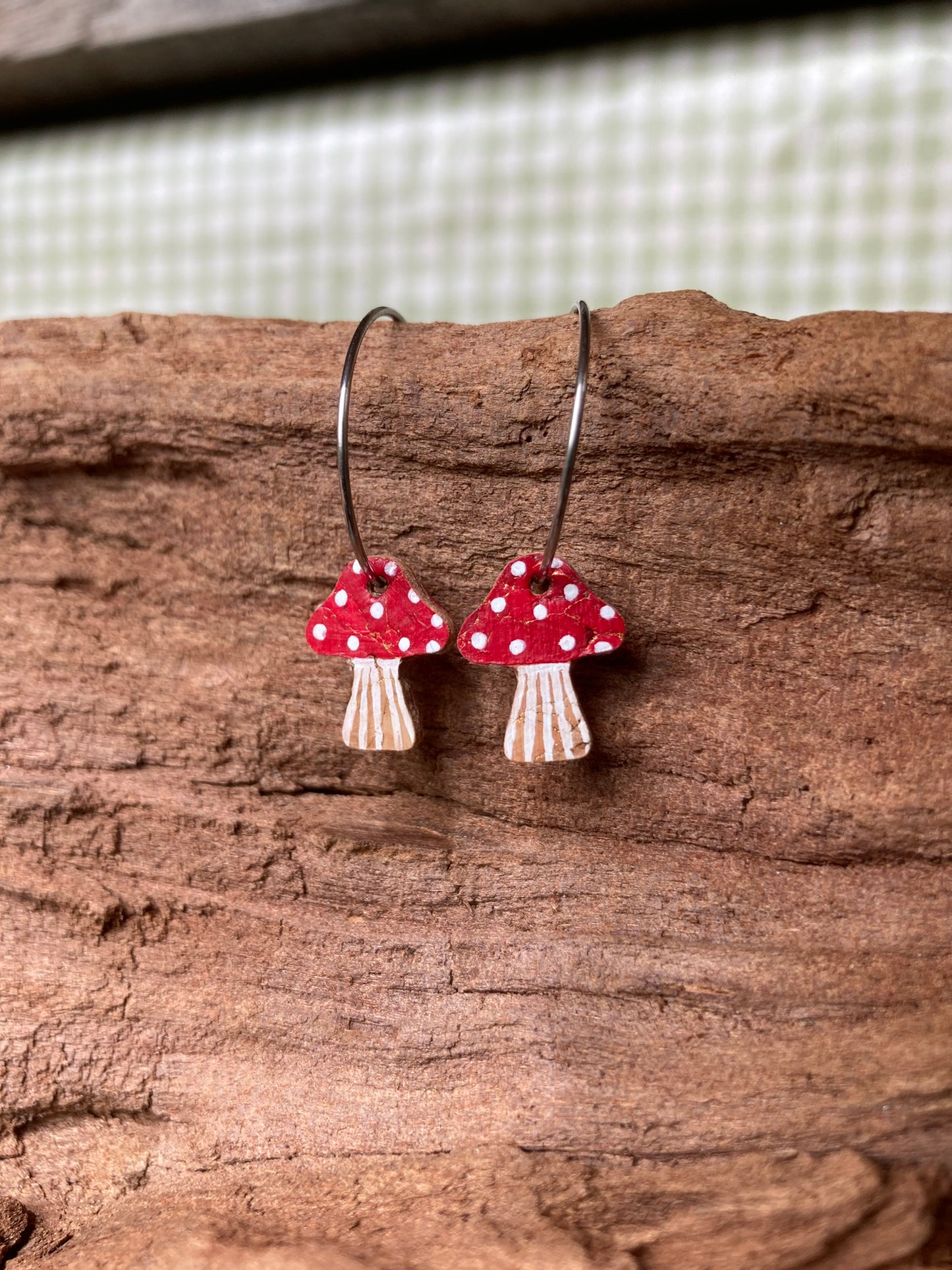 Mushroom-shaped earrings with red caps and white spots on a wooden surface