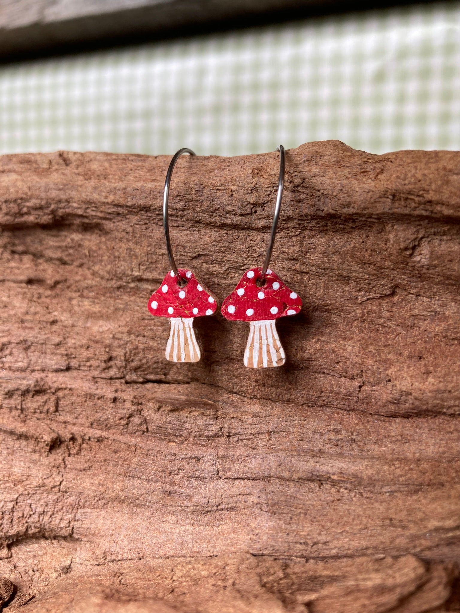 Mushroom-shaped earrings with red caps and white spots on a wooden surface