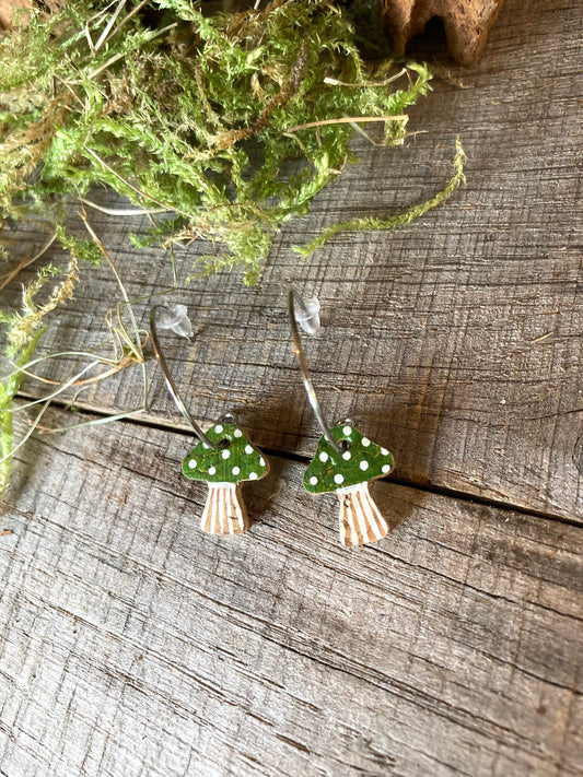 Mushroom-shaped earrings with green caps and white spots on a wooden surface.