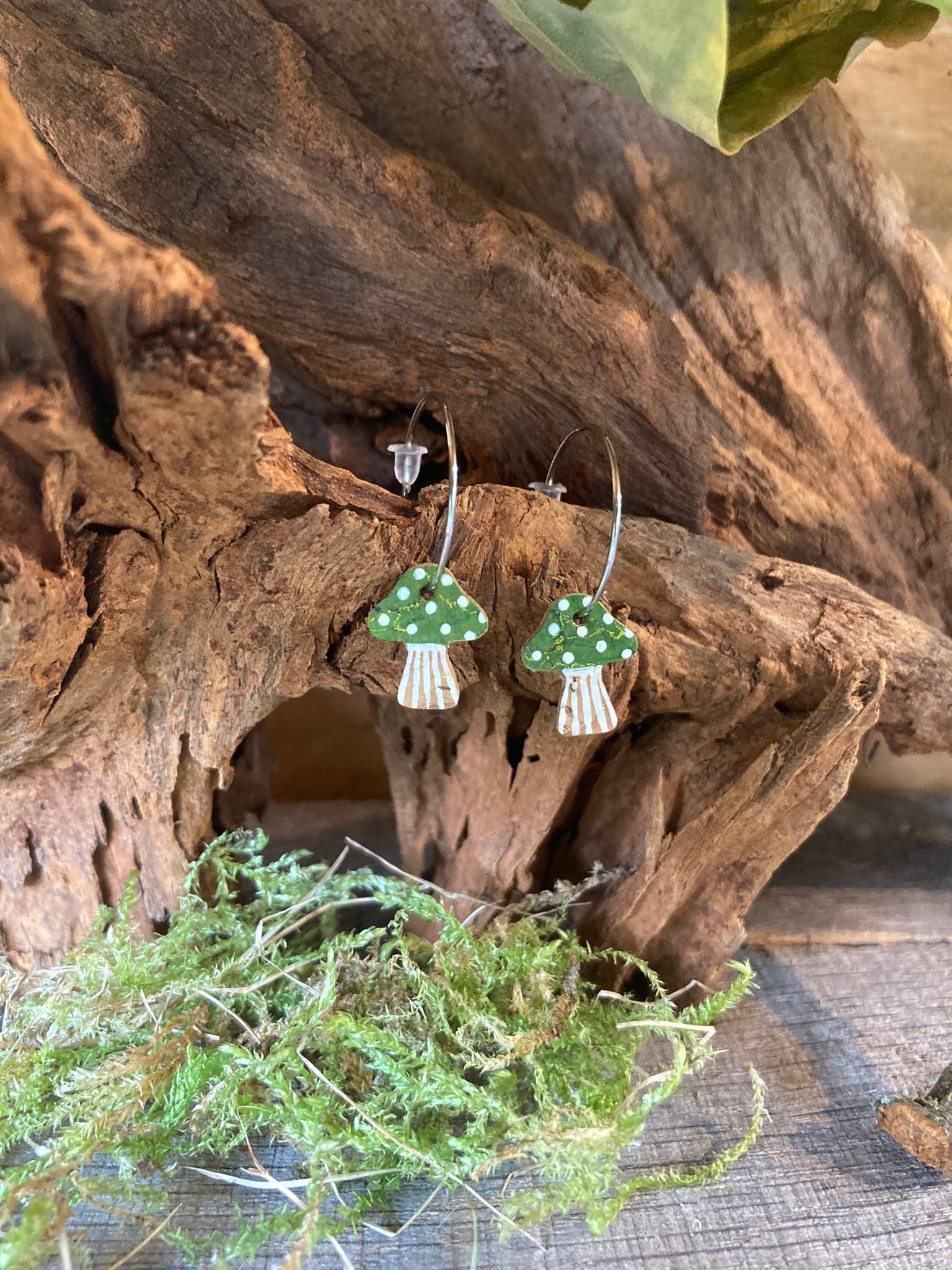 Green mushroom-shaped earrings on a wooden surface with foliage