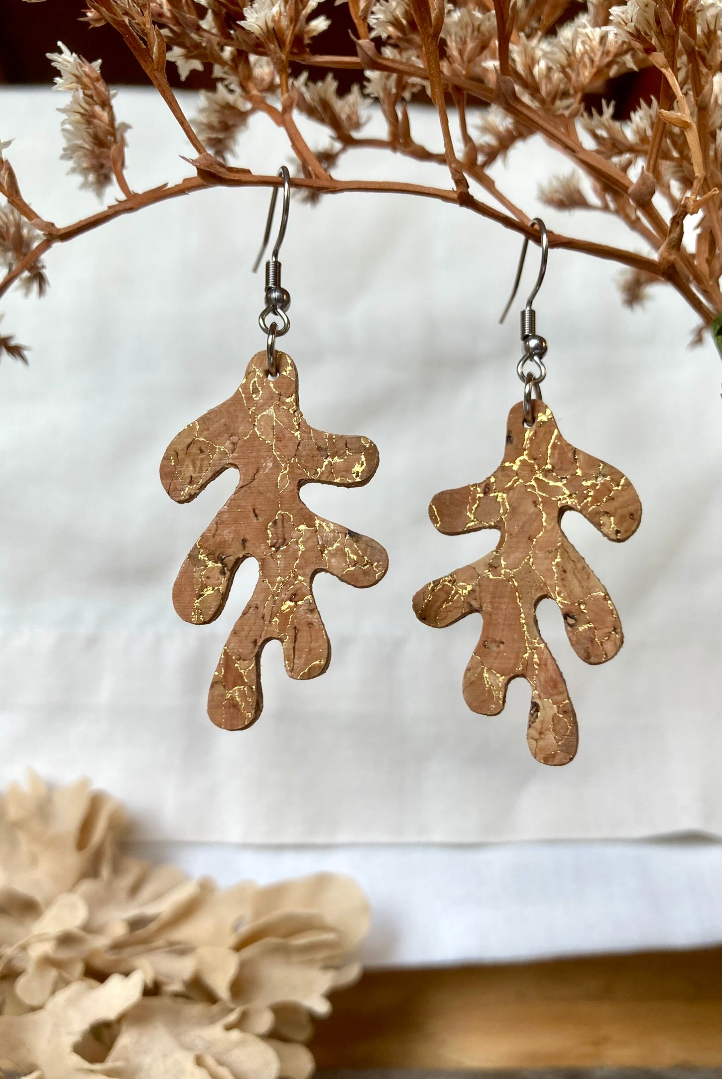 Gold flecked cork abstract leaf shaped earrings on a white background with dried flowers.