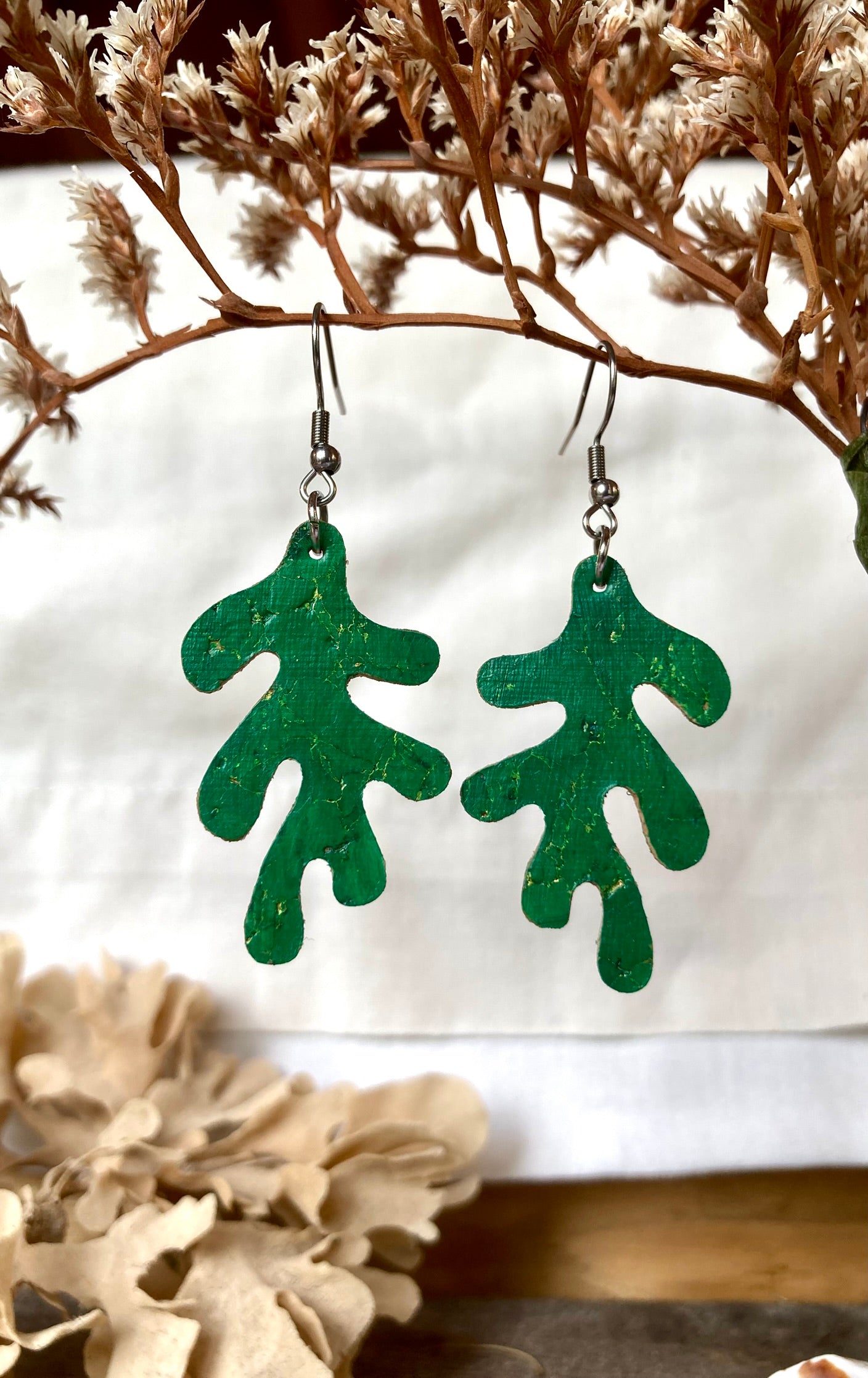Green leaf-shaped earrings on a white background with dried flowers.