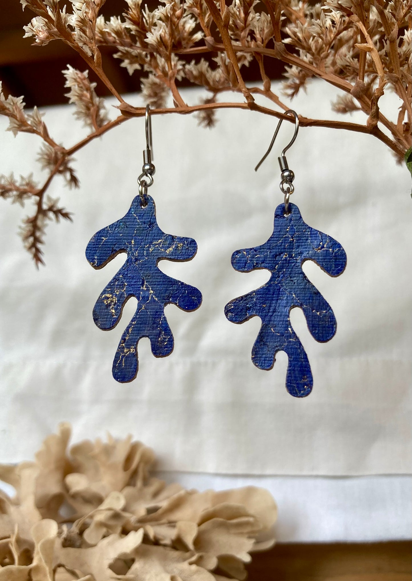 Blue coral-shaped earrings on a white background with dried plants.