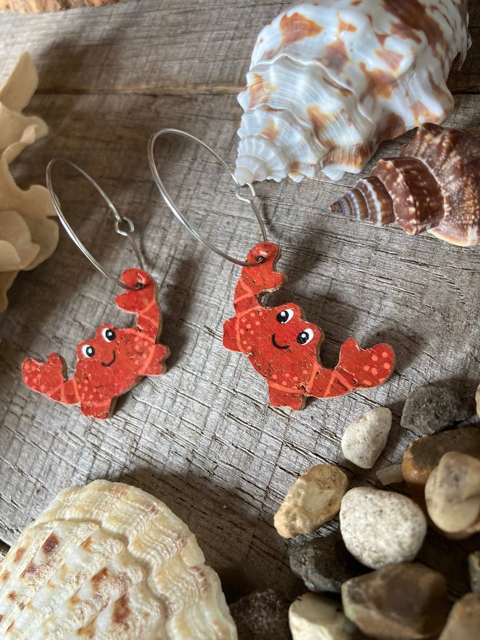 Red happy crab-shaped earrings on a wooden surface with seashells and stones.
