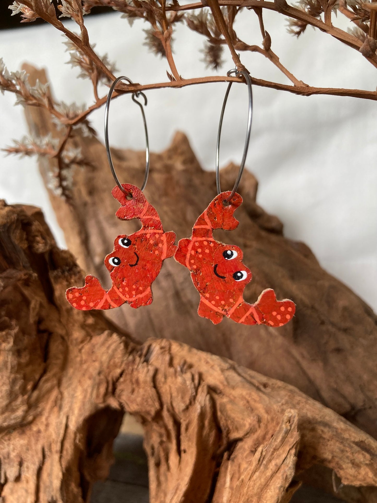 Red crab-shaped earrings on silver hoop earrings against a natural background.