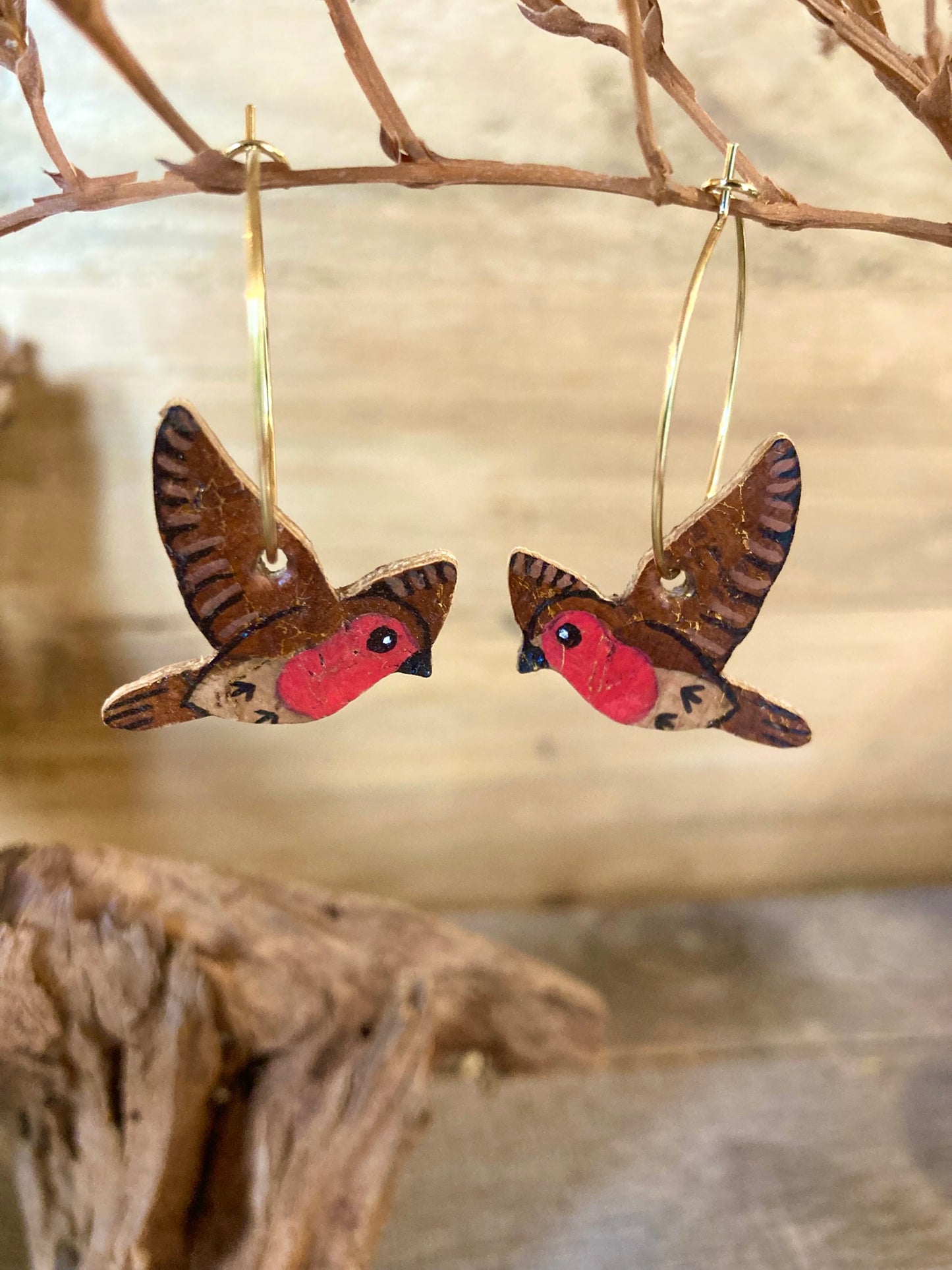 Handpainted robin earrings hanging from a branch with a natural background
