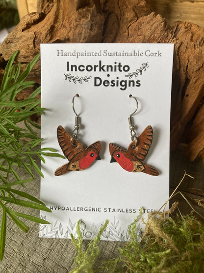 Bird-shaped earrings on a card with 'Incorknito Designs' branding, surrounded by natural elements.
