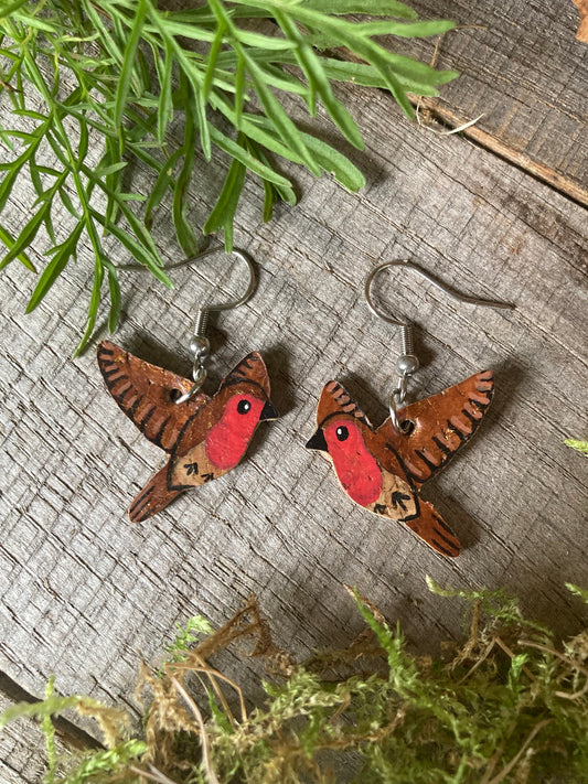 Handpainted robin cork earrings earrings on a wooden surface with greenery.
