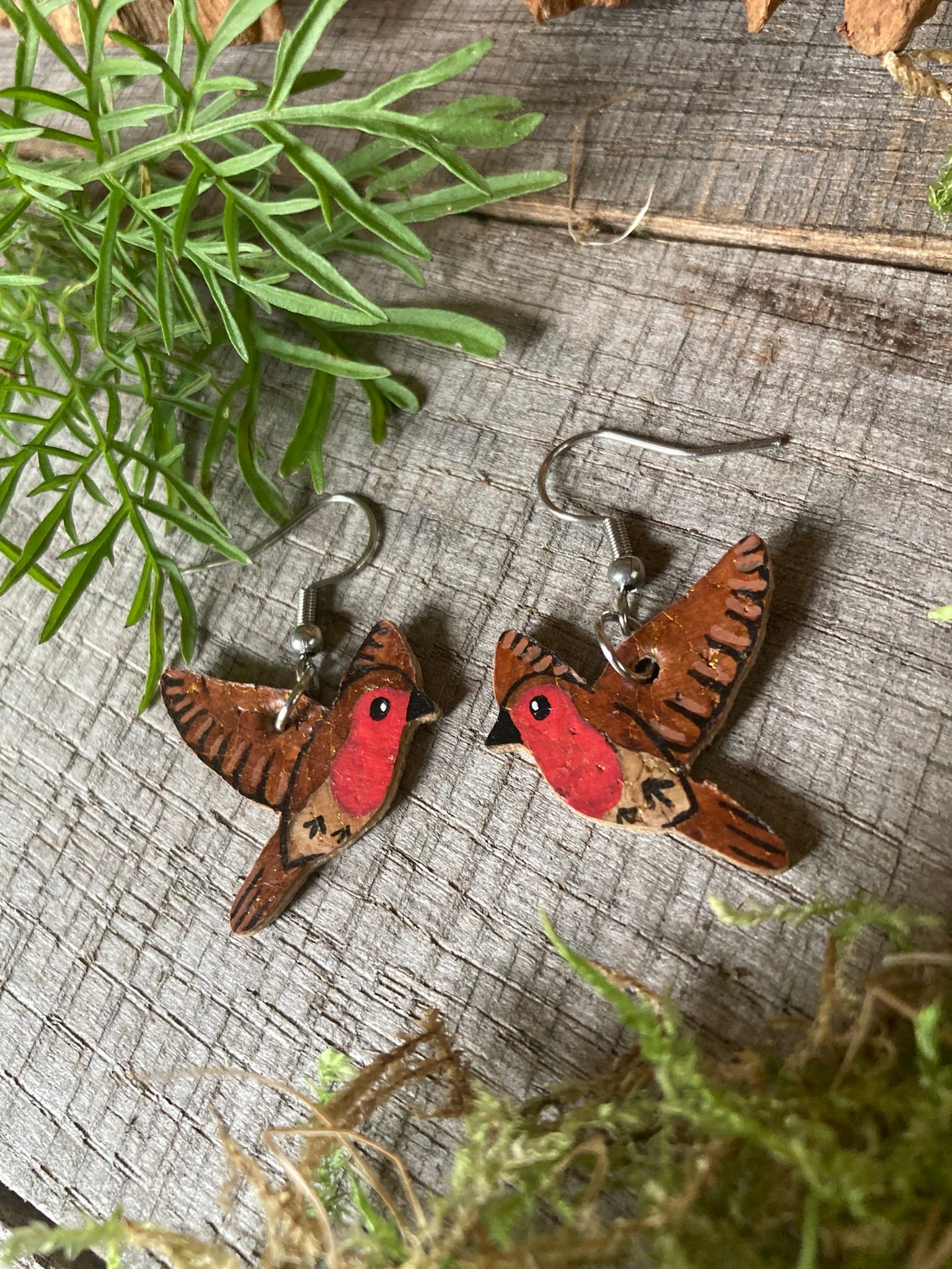 Cork bird-shaped earrings on a wooden surface with greenery