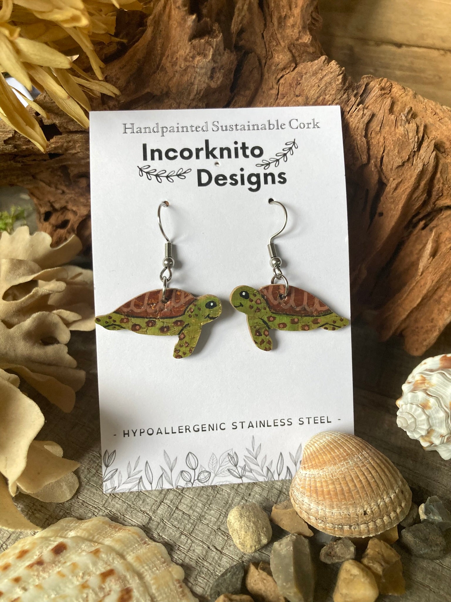 Turtle-shaped earrings on a 'Incorknito Designs' card with natural elements in the background