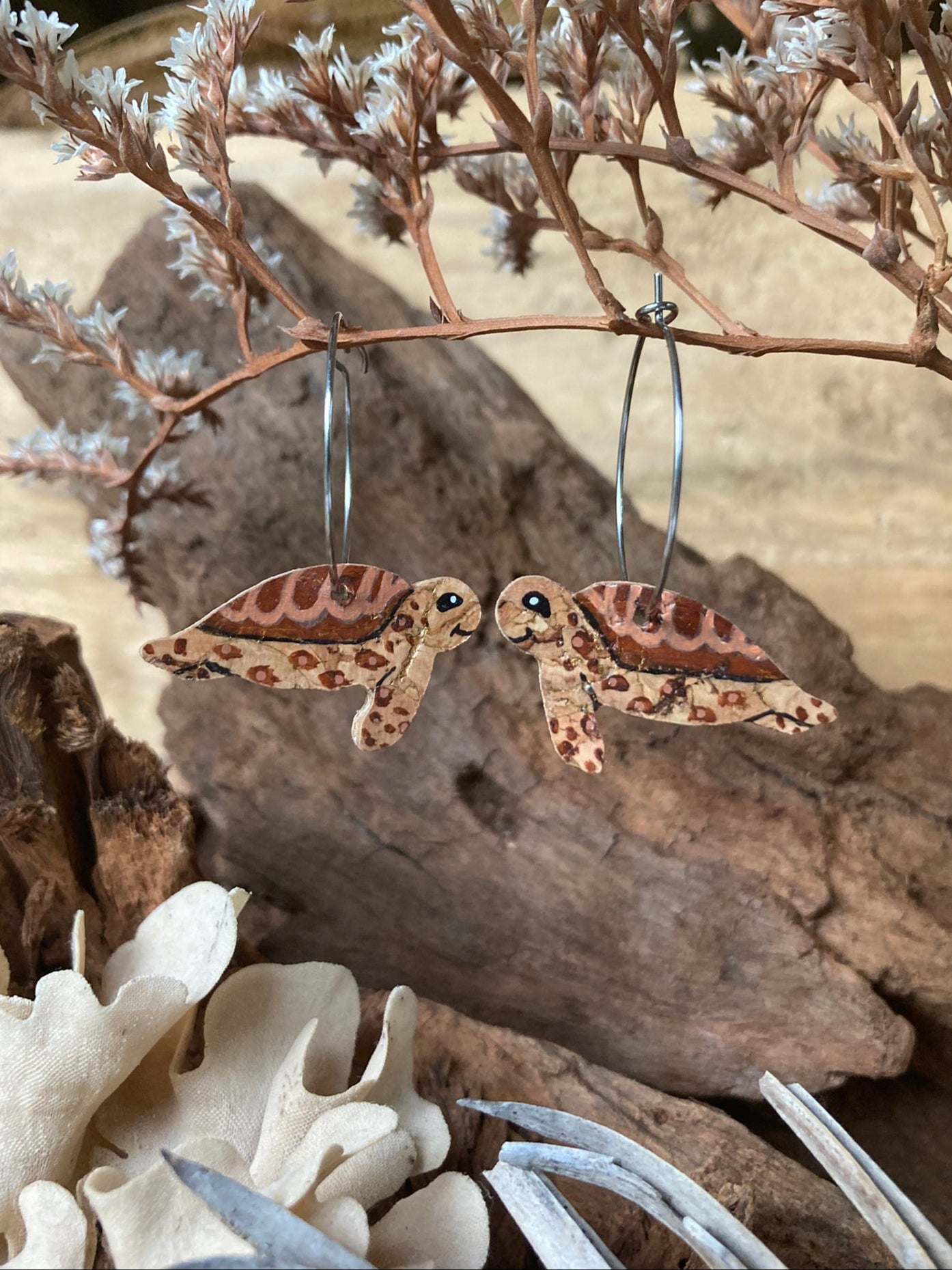Pair of brown turtle-shaped earrings on a natural background with dried plants.