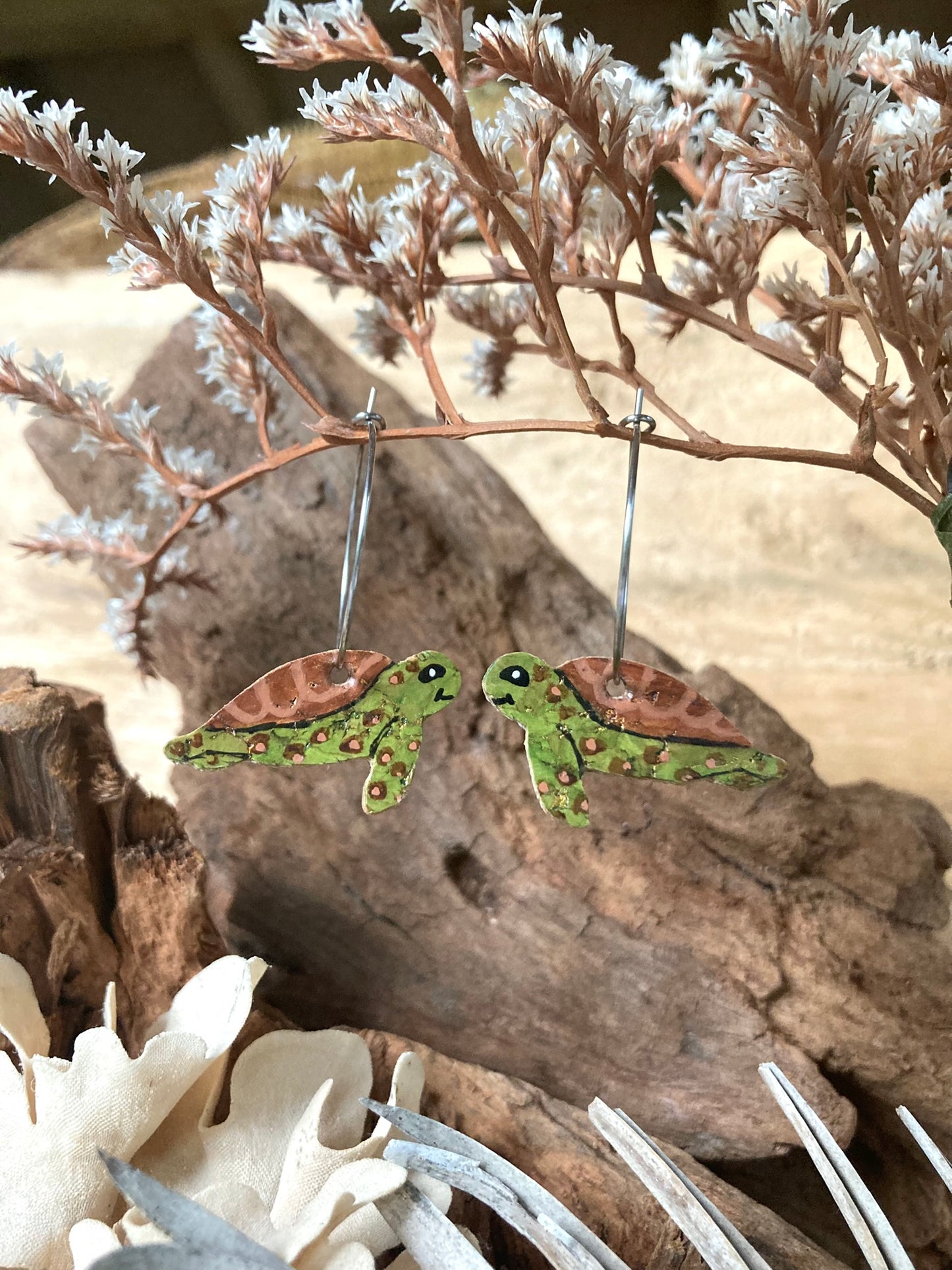 Pair of turtle-shaped earrings on a natural background with dried plants.