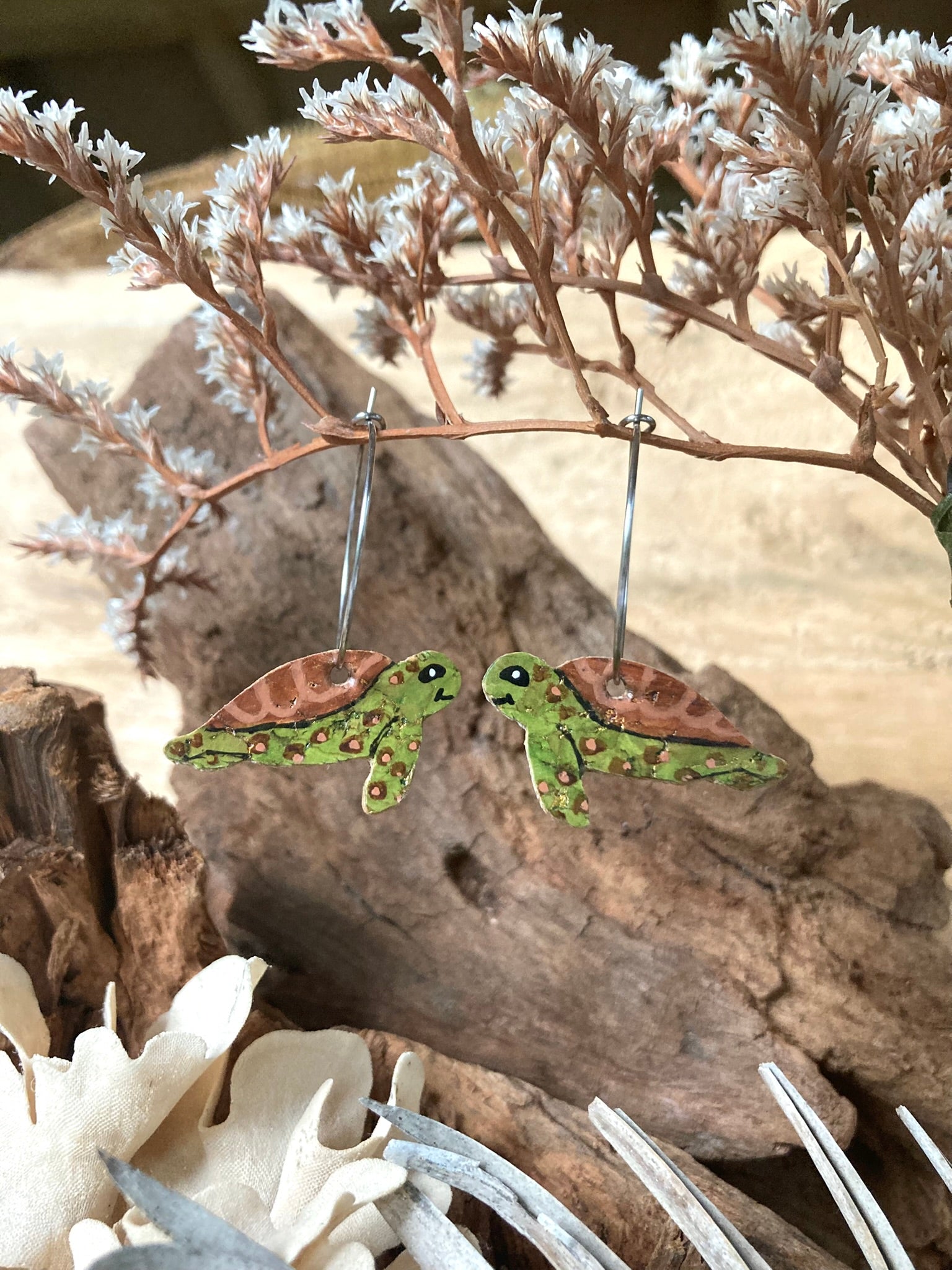 Pair of turtle-shaped earrings on a natural background with dried plants.