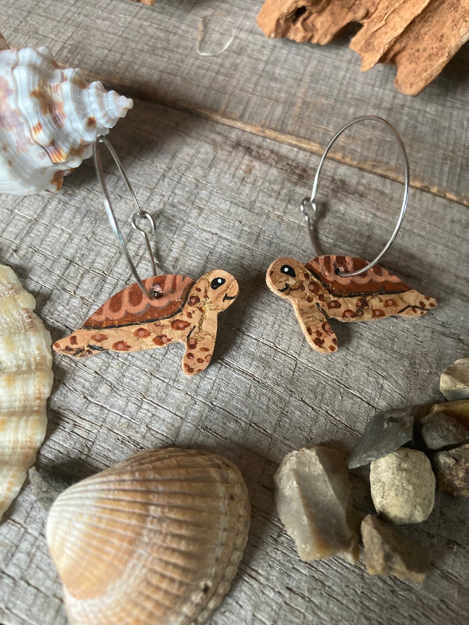 Turtle-shaped earrings on a textured surface with shells and stones.