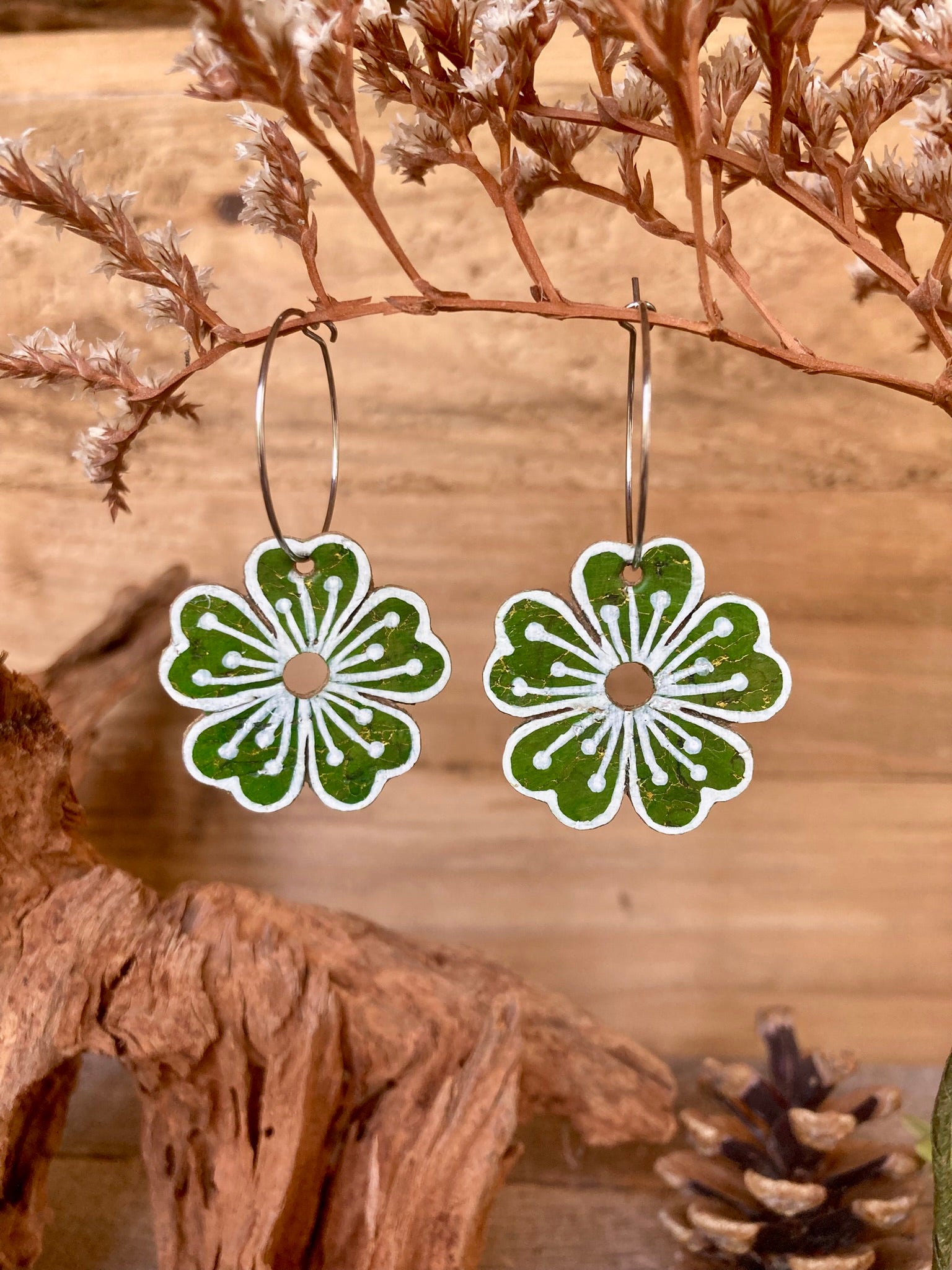 Bold green flower earrings on a wooden branch with dried leaves and pinecones.