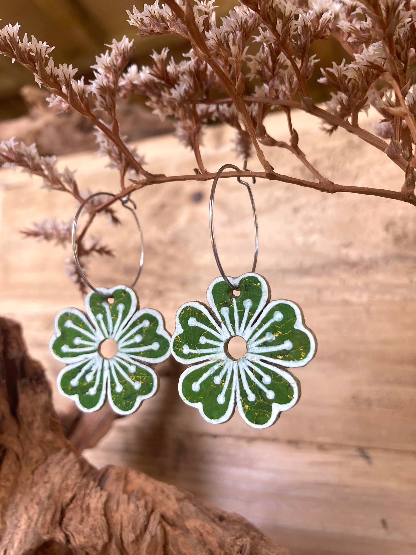 Green floral earrings on a wooden surface with dried plants.
