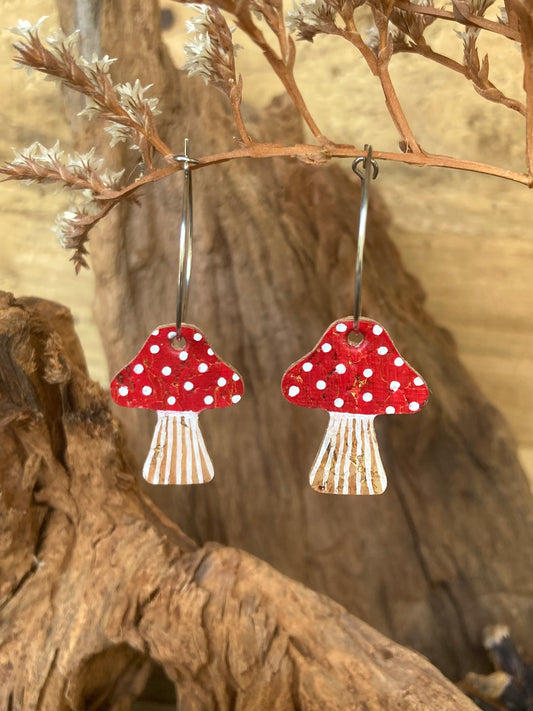Red mushroom-shaped cork earrings with white polka dots hanging on a branch.