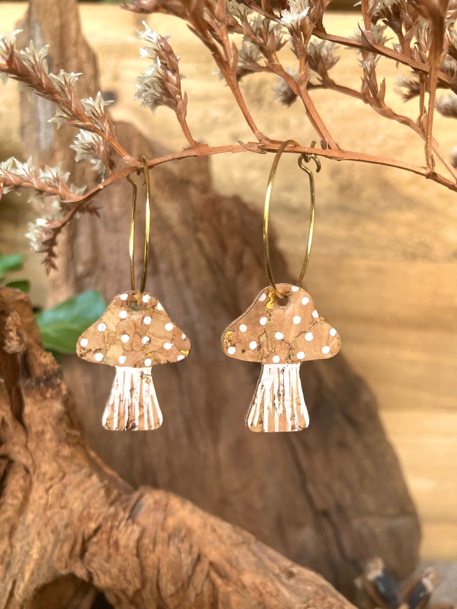 Gold flecked mushroom-shaped natural cork earrings on a branch with dried leaves