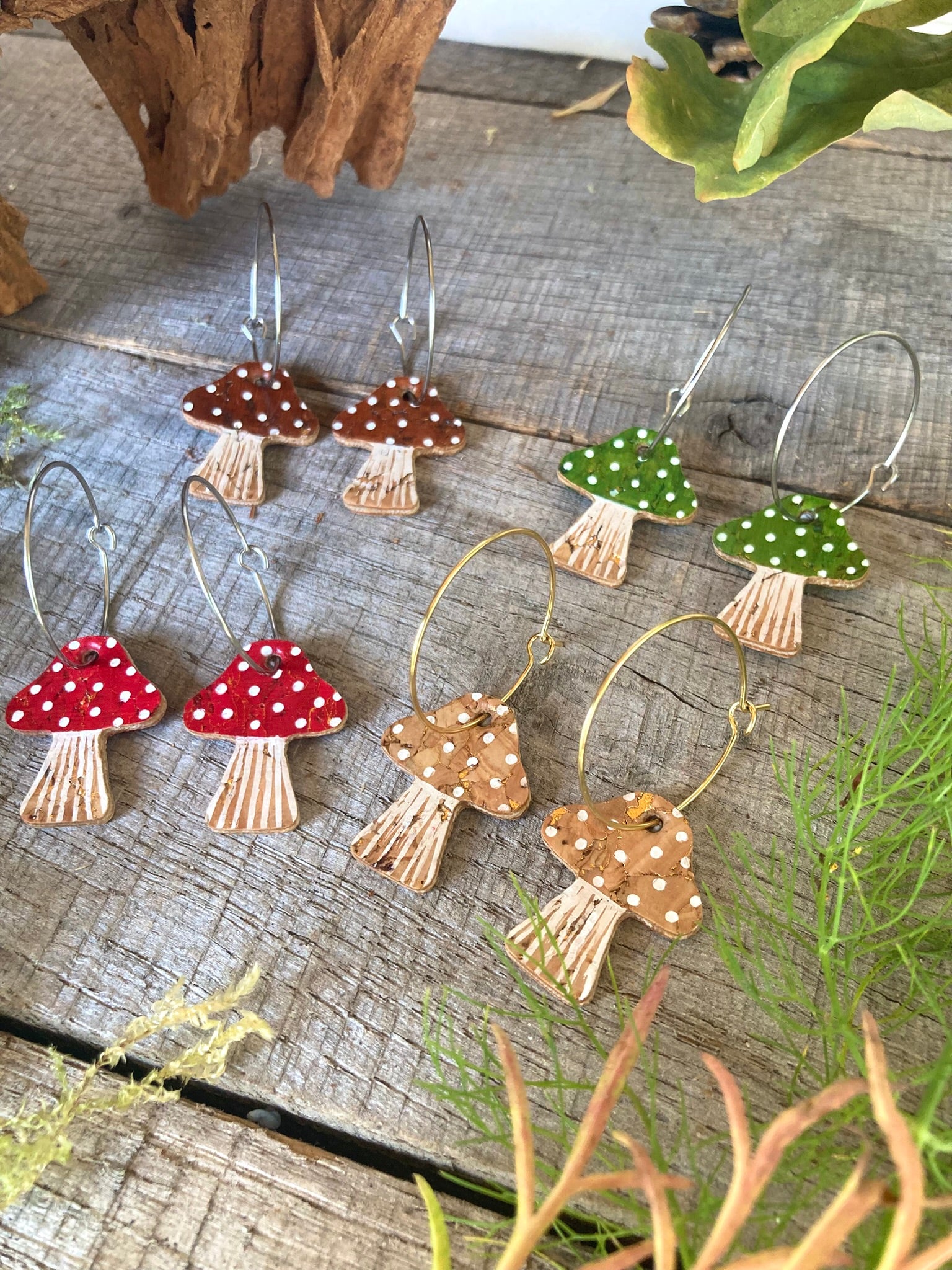 Mushroom-shaped earrings on a wooden surface with plants around