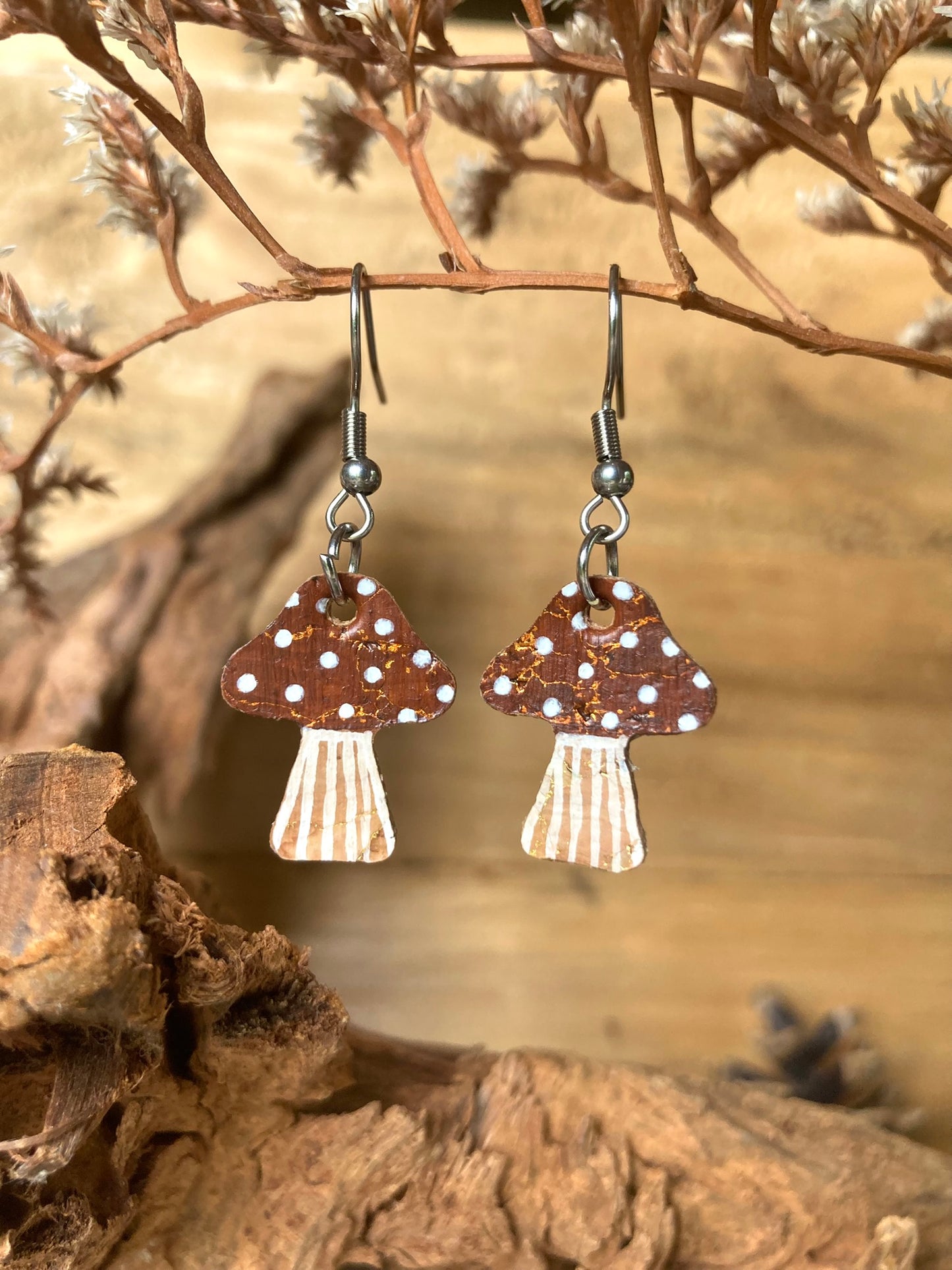 Brown toadstool earrings with white spots on a natural wood and branch background