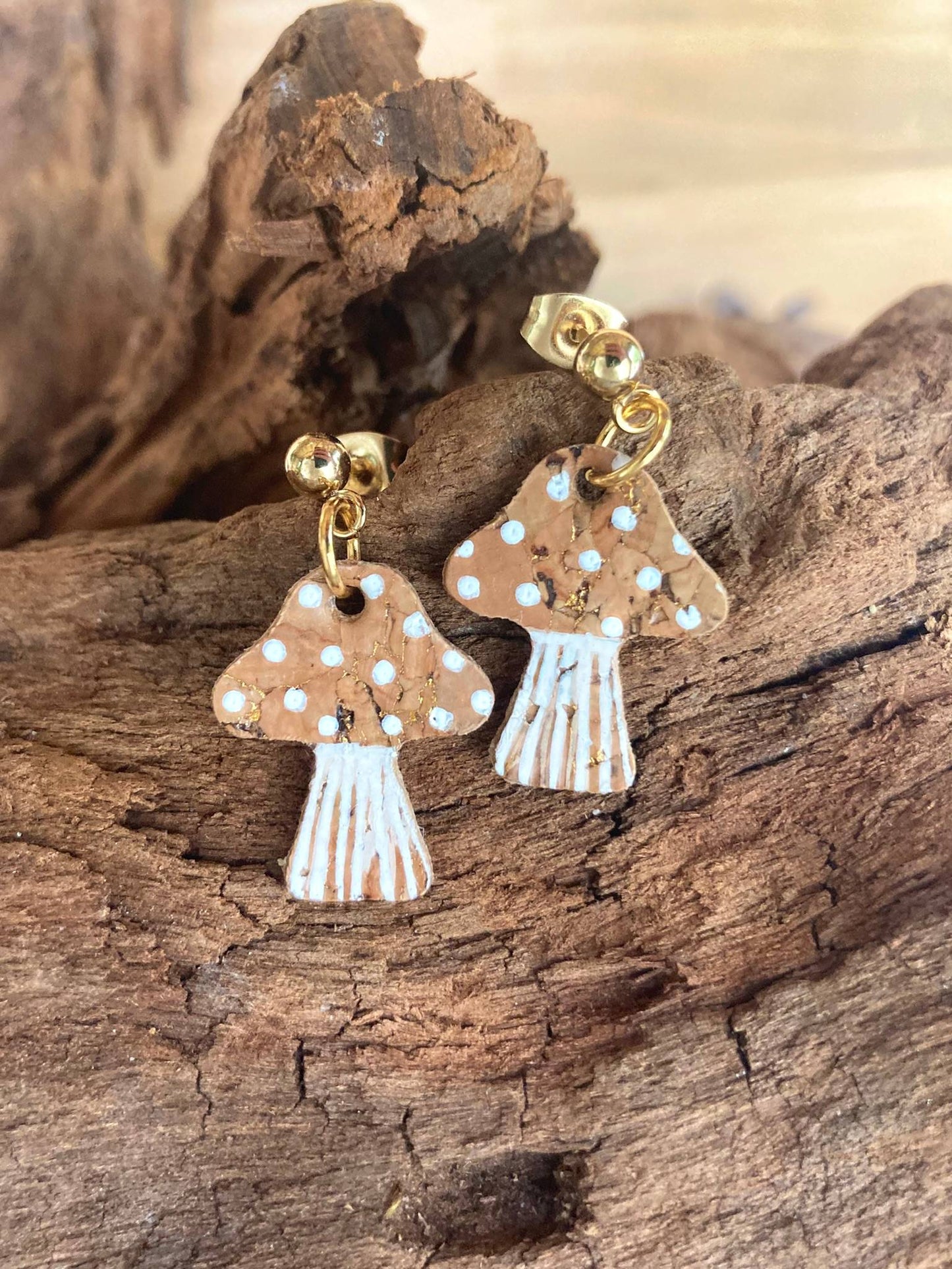 Beige toadstool-shaped earrings with gold accents and white detailing on a wooden surface