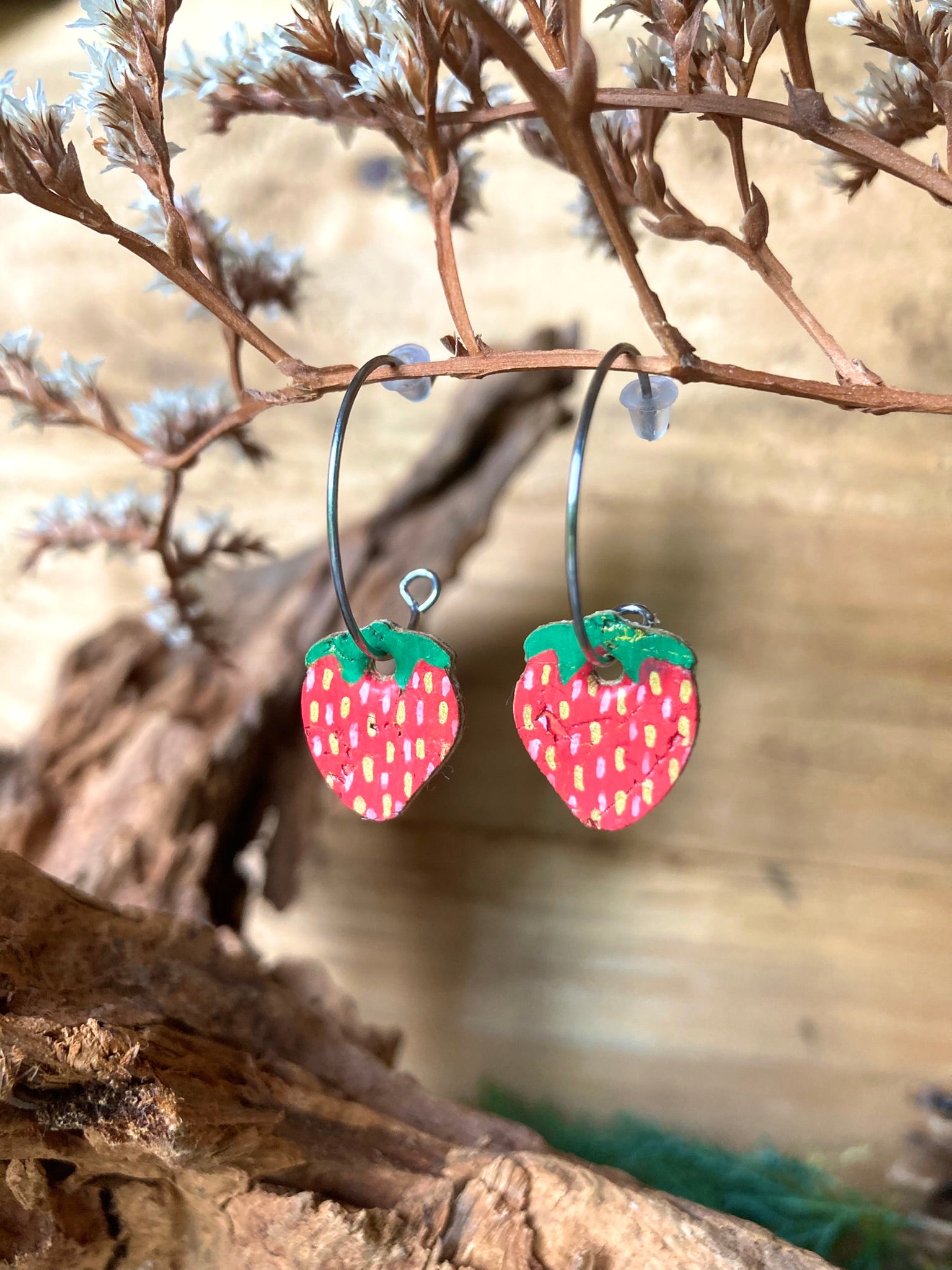 Strawberry-shaped earrings on a branch with a blurred natural background