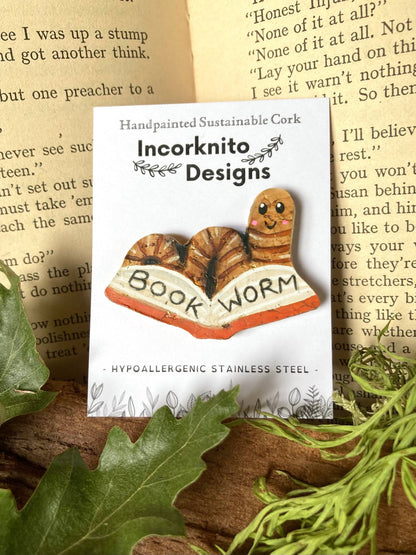 Cork brooch shaped like a bookworm on a card with 'Incorknito Designs' branding, set against a textured paper background.
