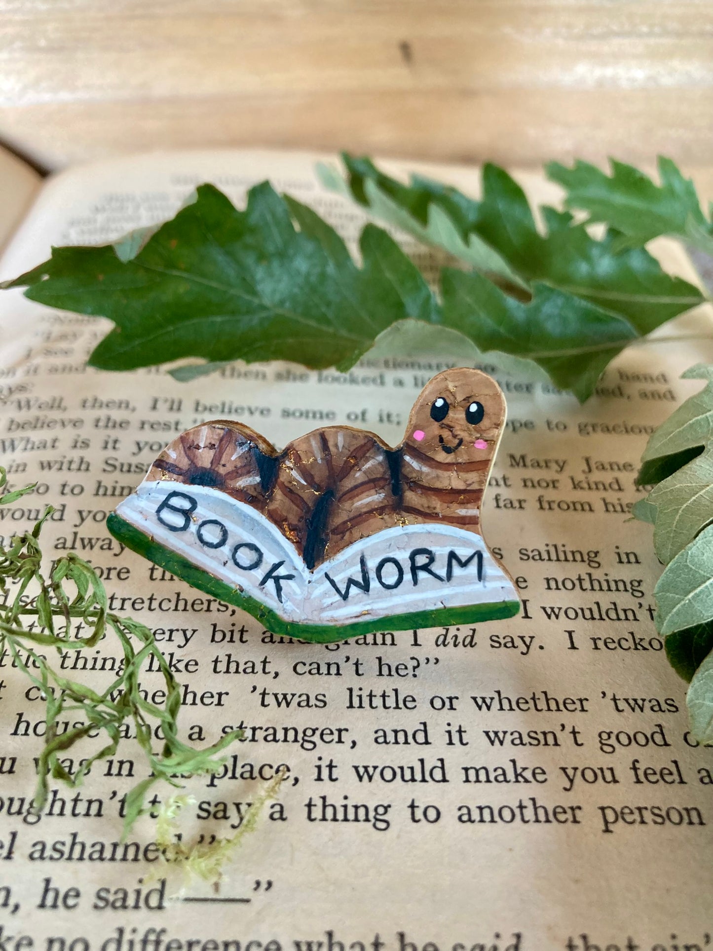 Decorative pin badge with 'Book Worm' text on an open book with leaves.