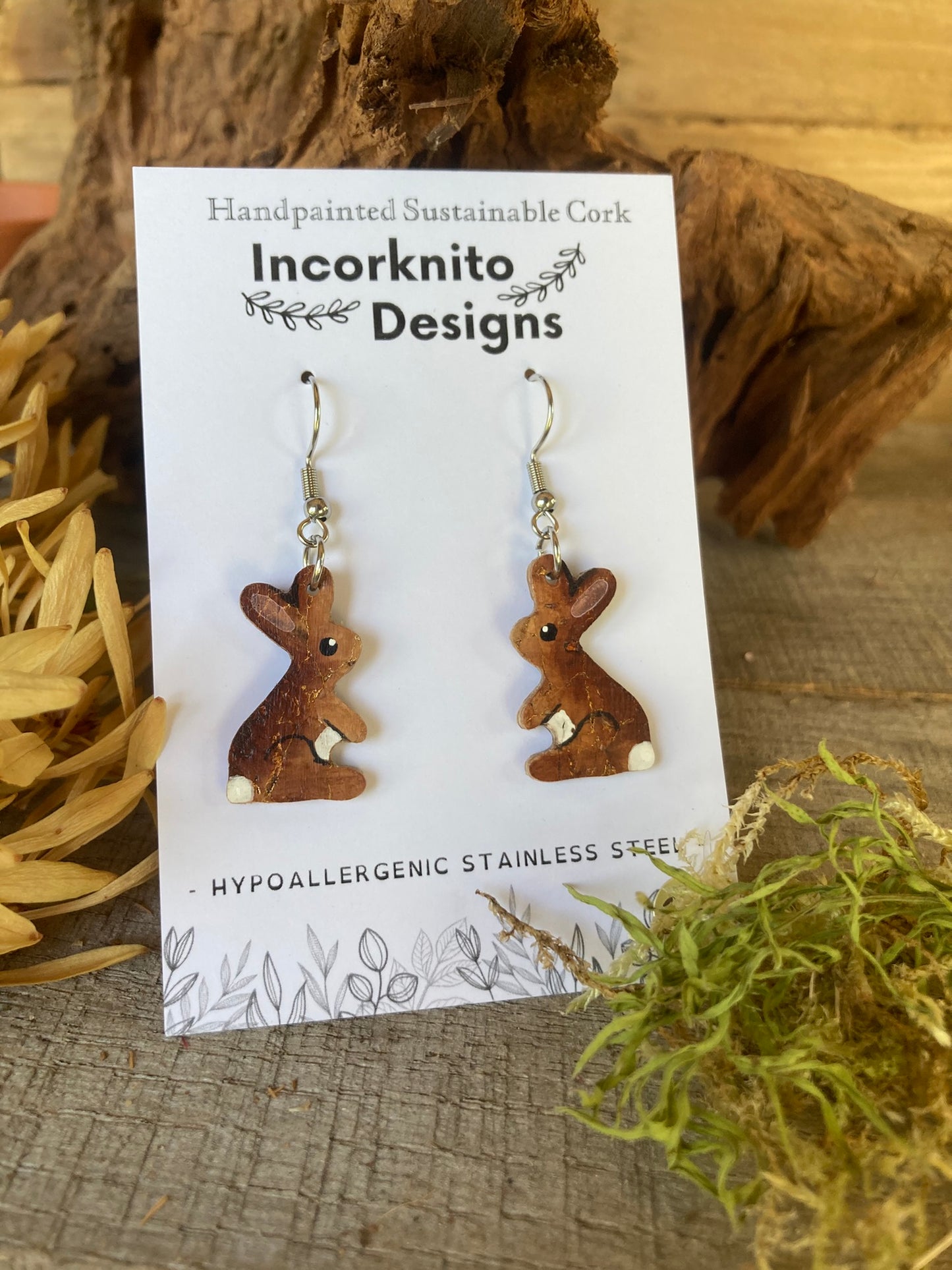 Bunny-shaped earrings on a card with 'Incorknito Designs' branding, placed on a wooden surface.