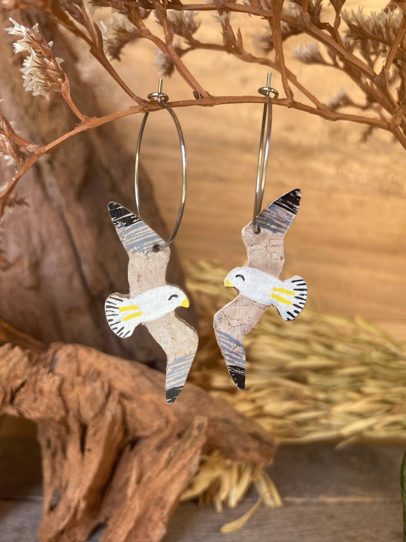 Seagull earrings with little yellow legs and beak made from cork hanging from a natural branch
